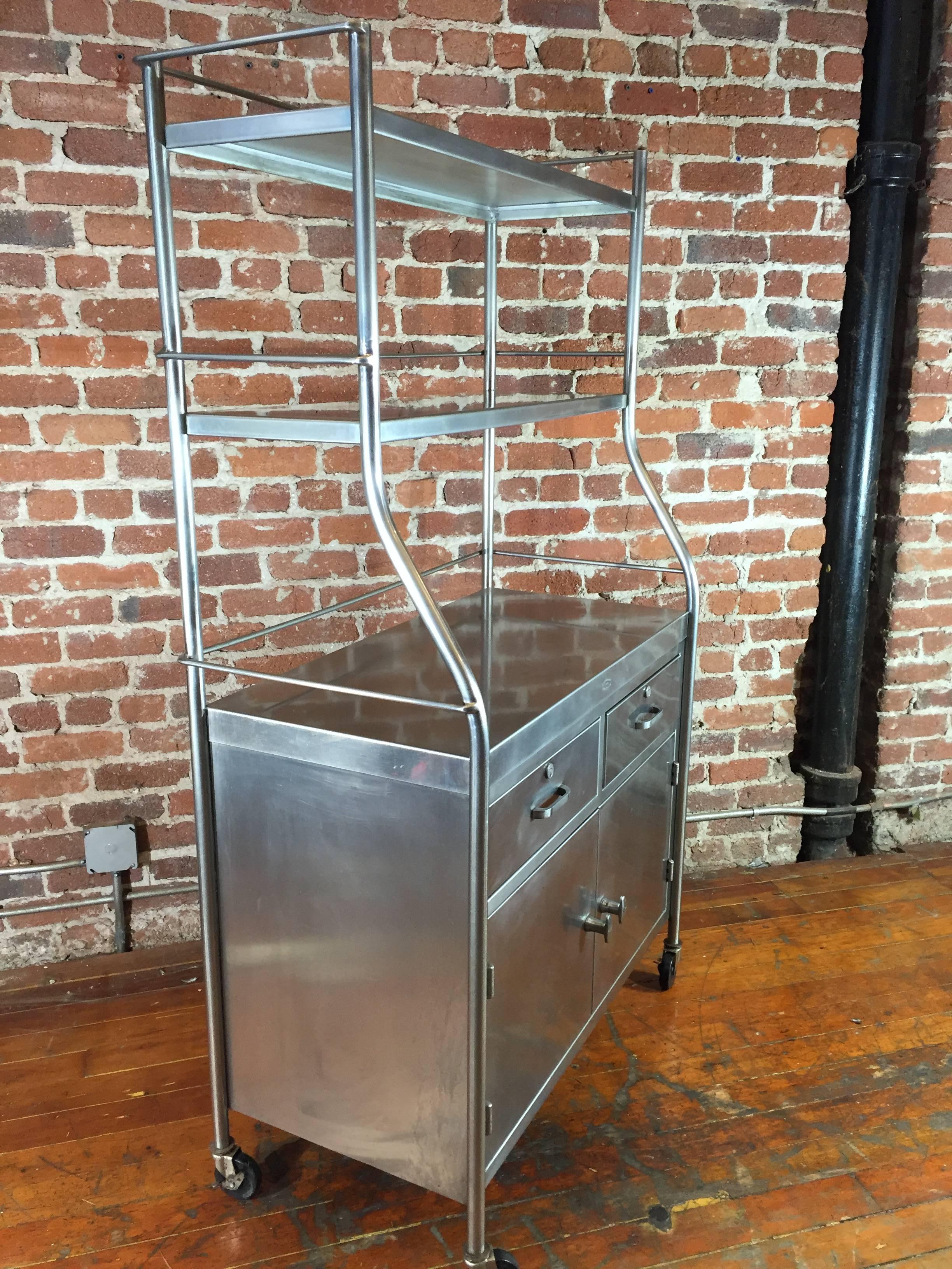 Excellent quality stainless steel utility cabinet. This piece features 2 drawers, lower cabinet storage, and open upper shelves. Surface height is 32