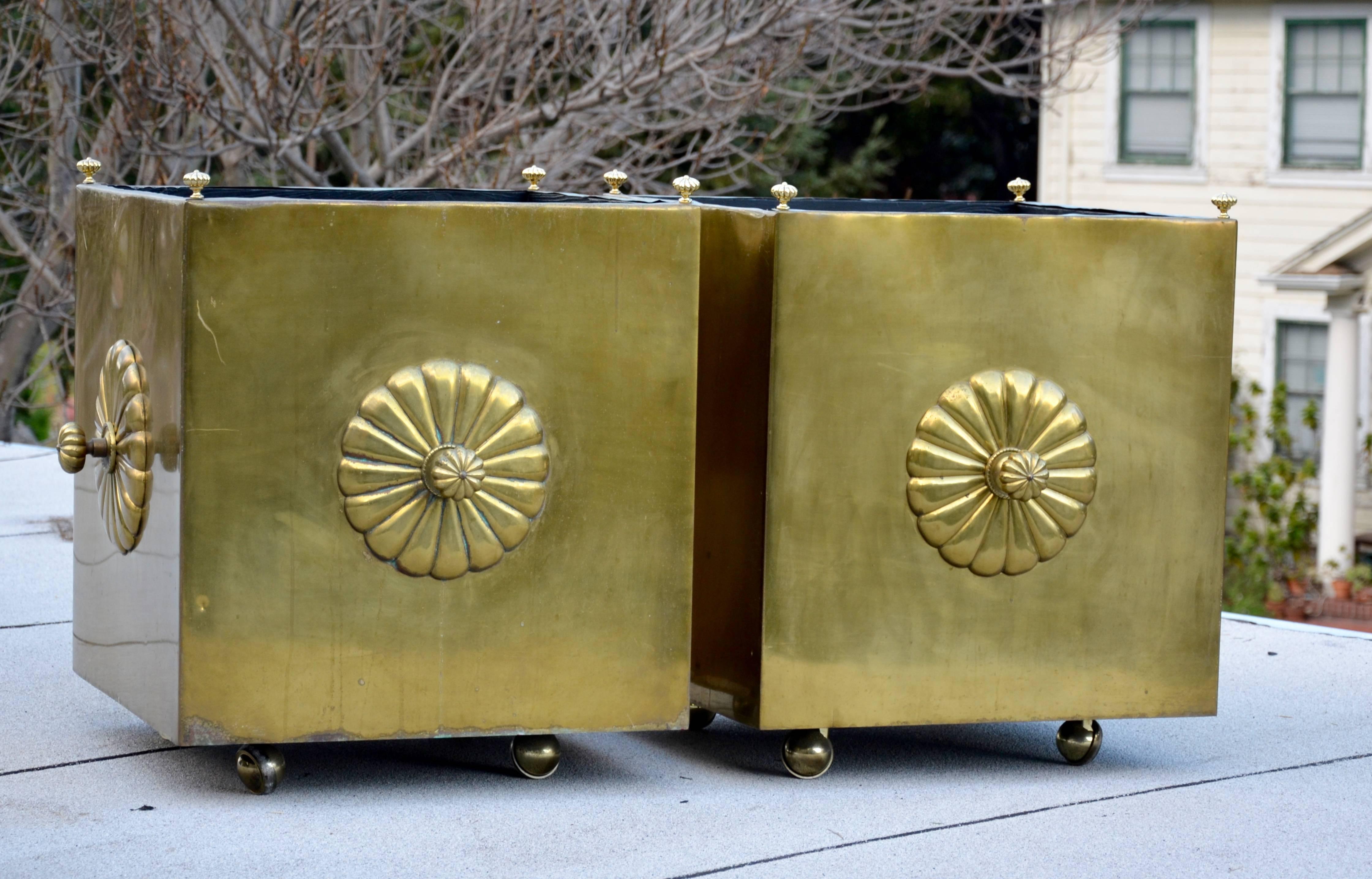 These fabulously decorative pair of brass planters are comprised of solid heavy gauge brass, veneered to sturdy wood box frames. Nicely detailed with scalloped medallions and brass finials. Casters were added for easy transport. We can polish them