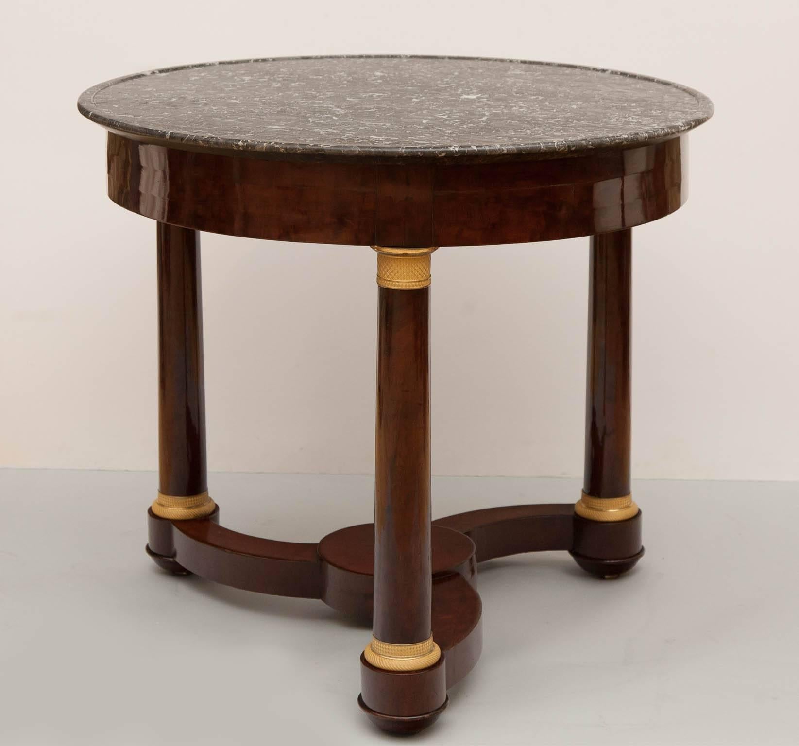Mahogany and mahogany veneer gueridon on three legs with a triform base. 
Finely incised gilt bronze mounts, a grey and white marble top with a 'cuvette' edge. 
France c. 1820.