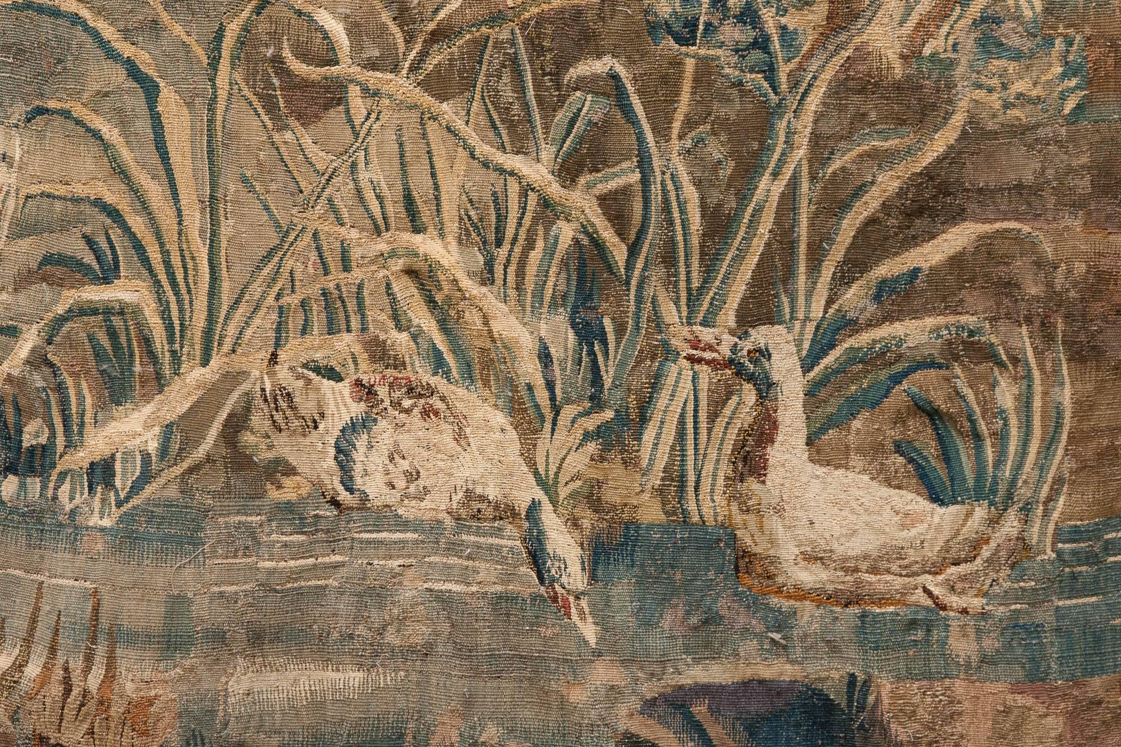 Verdure tapestry with a large house in the distance and a river flowing to the foreground with two ducks swimming.
With poppies, trees and bull rushes on the river bank. Surrounded by a floral border.
Woven in wool and silk, France, circa 1760.