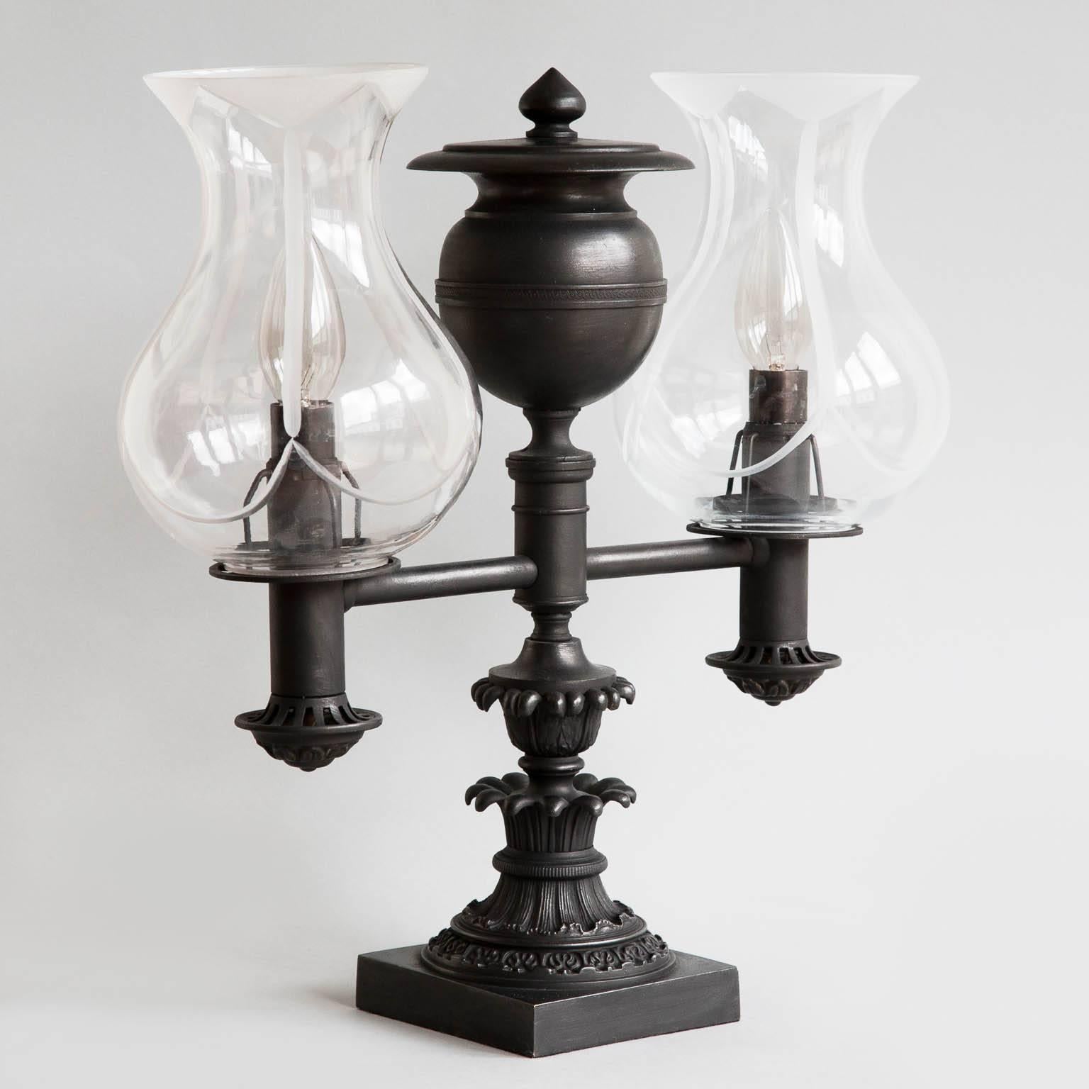 The central column with cast foliate decoration, surmounted by an urn with a pointed finial on top. Each with two straight arms and single burners, now currently electrified for the UK with E14 bulb holders. 
With later replacement glass shades,