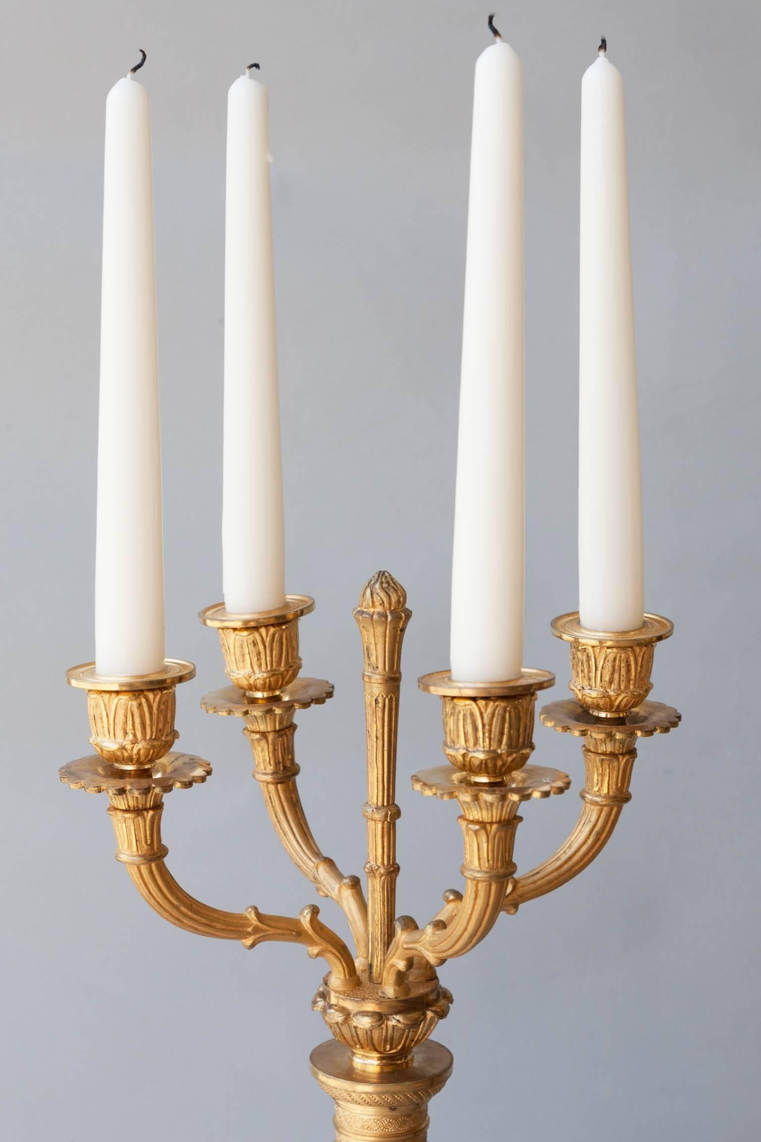 Four gilt bronze fluted arms with one central fluted column.
The central patinated bronze columns with gilt leaf and berry twisting mounts. Mounted on cylindrical plinths over square bases decorated with gilt swags and bows.
France, circa 1835.