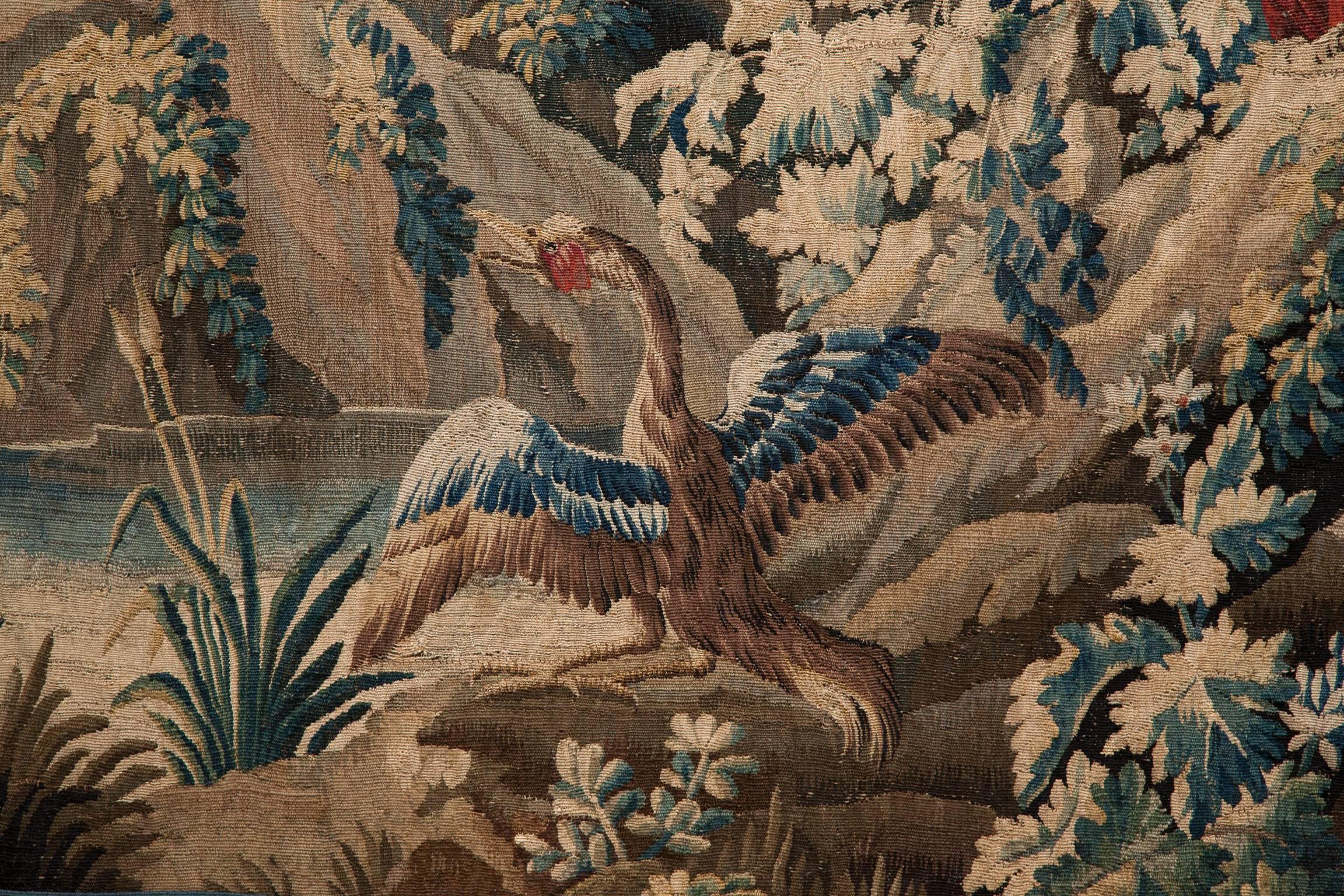 Woven with a three sided blue and red patterned border decorated with twisting acanthus leaves and flowers.
With an exotic bird in the foreground contemplating a pool of water, and a parrot perched on a rock nearby. In the distance a pagoda stands