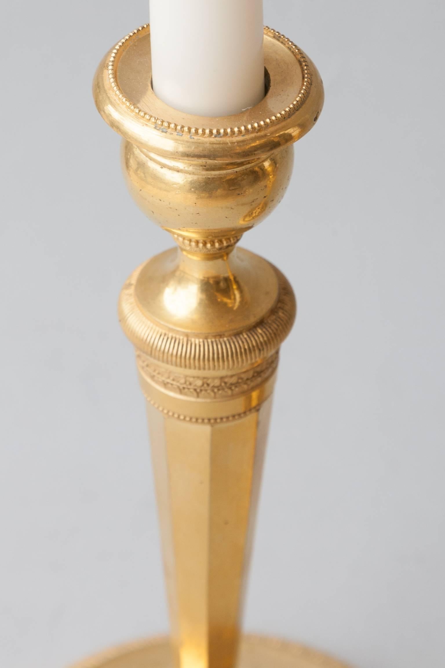 Pair of early 19th century ormolu candlesticks with octagonal downward tapering columns terminating in paw feet 
and raised on circular plinths with excellent quality incising, France, circa 1800.
    