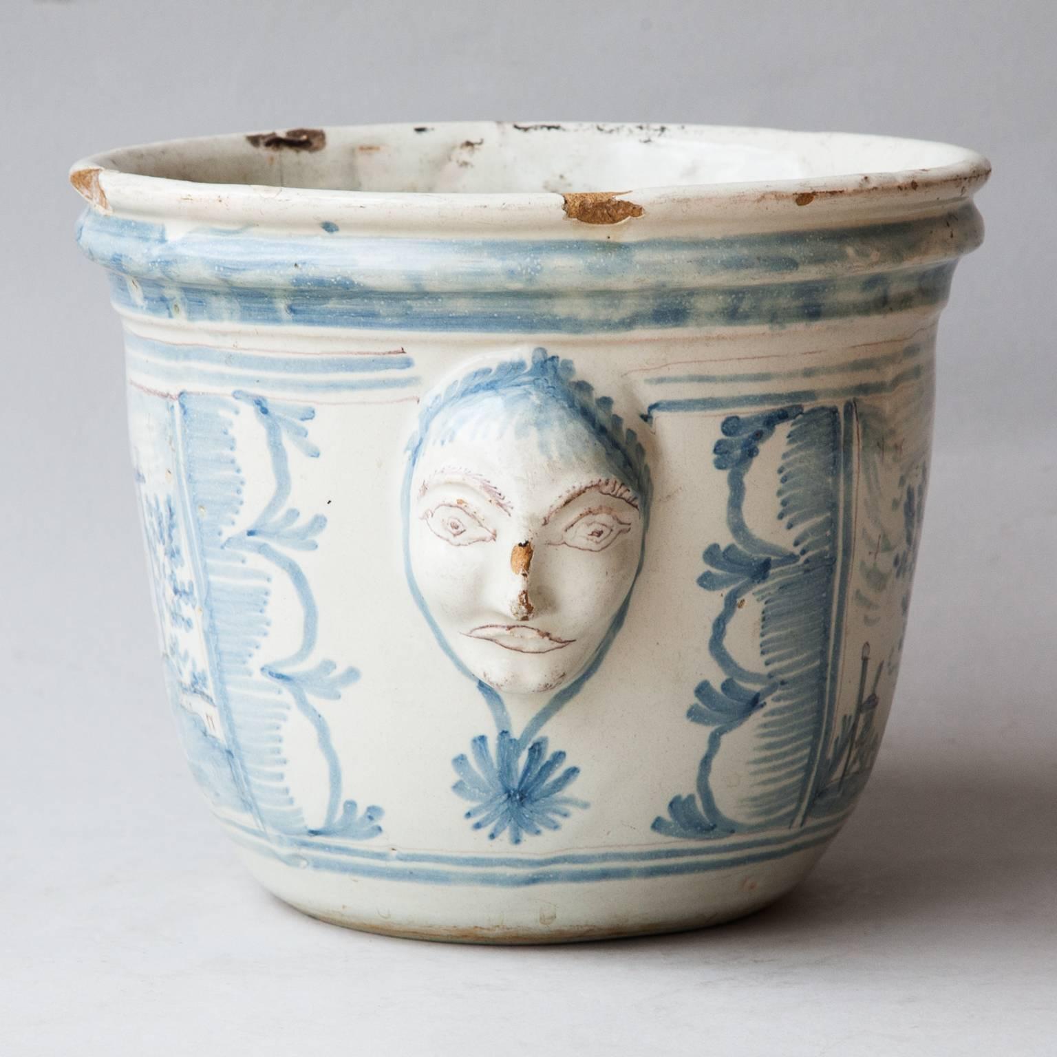 All blue and white cache pot or jardiniere with pastoral village scenes on either side and two mask handles.
A visible old repair on one side and other small chips and wear to the surface.
France, Nevers, 1760.