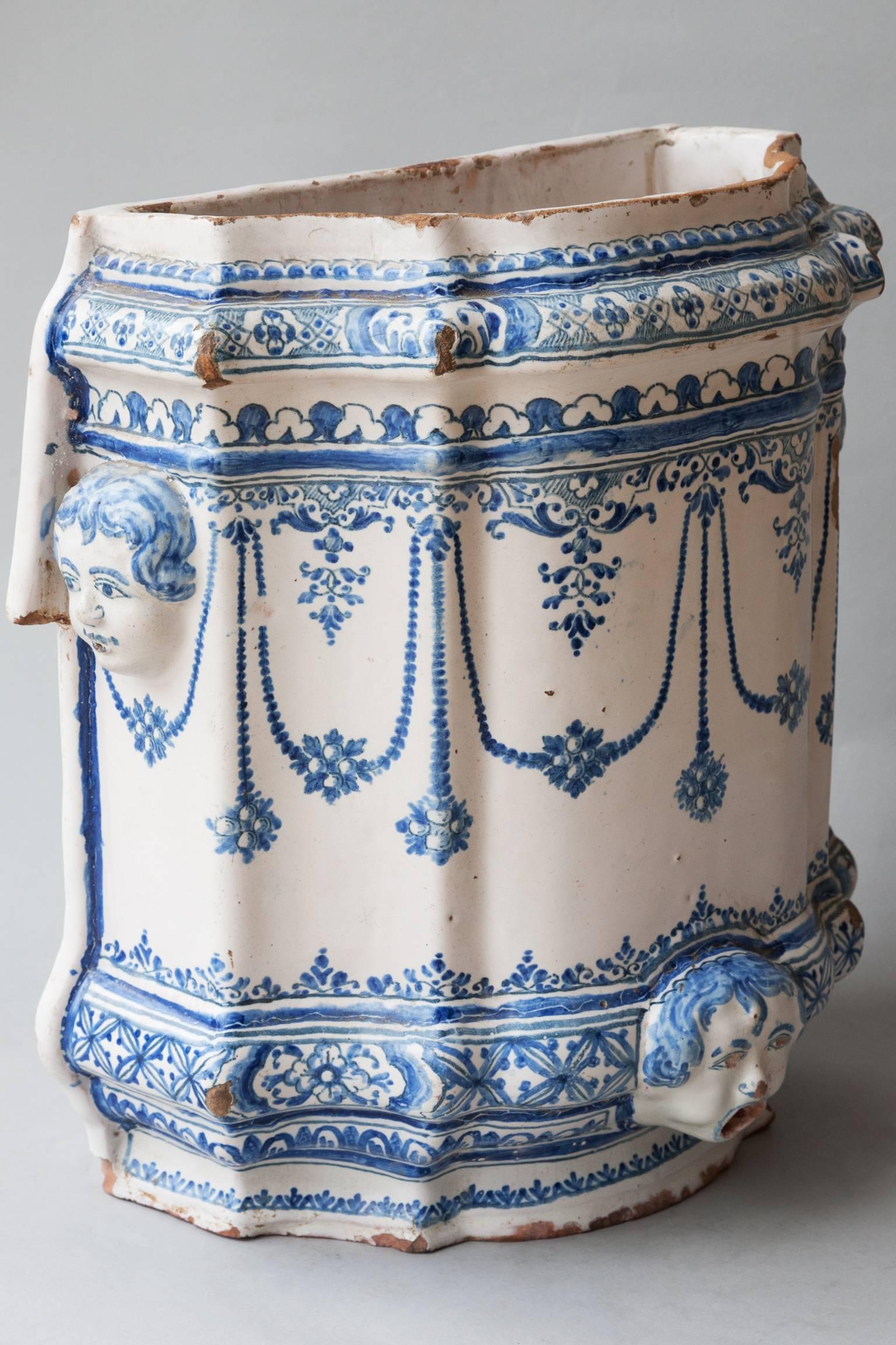 This blue and white faience corps was designed to be used inside for the dispensing of fresh water. With mask handles on either side and a mask at the base where there would have been a small tap coming from the mouth. Hand-painted with flowers and