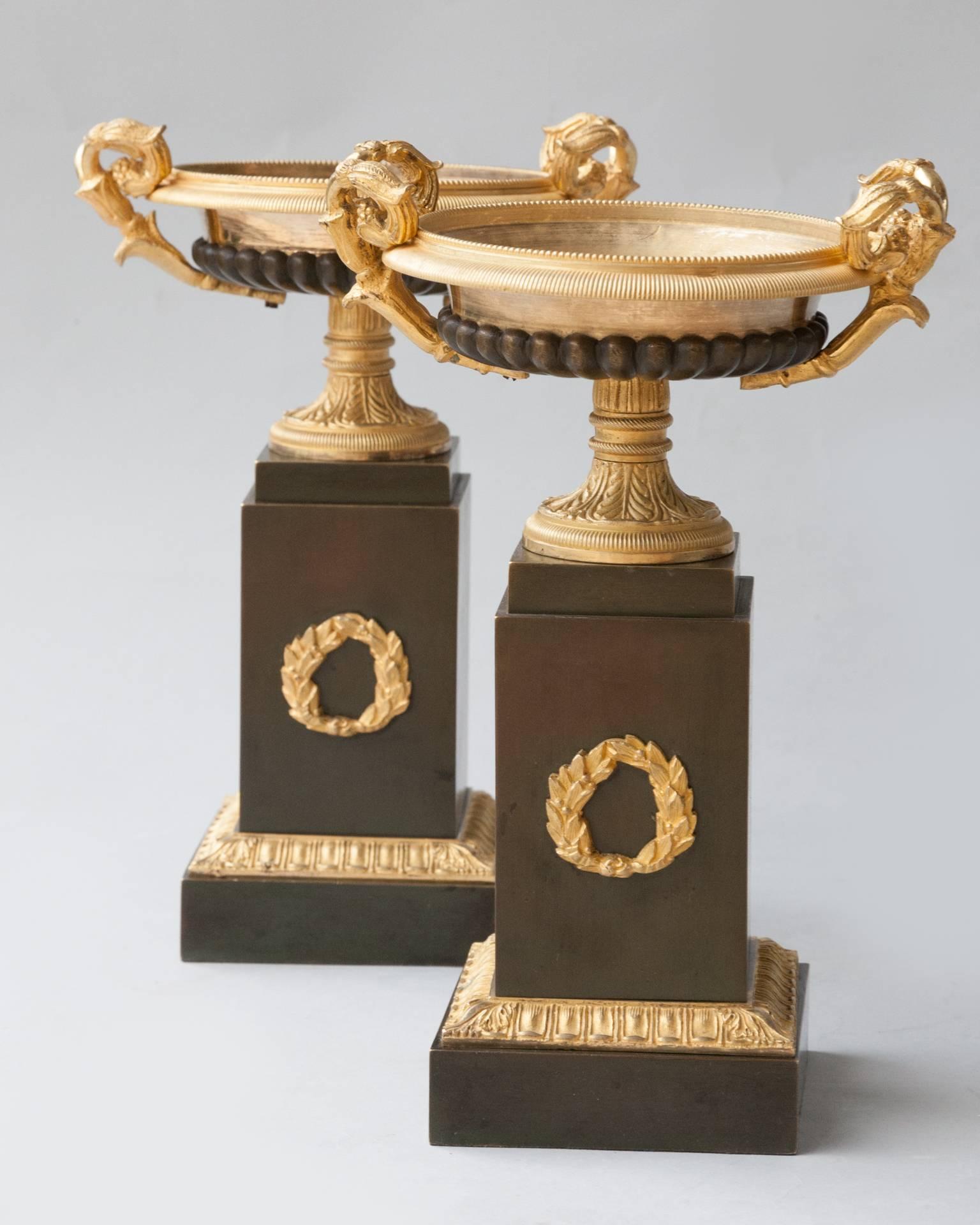 A pair of shallow gilt urns with a moulded and finely incised reeded edge over a patinated gadrooned body. The socle decorated with leaves and resting on a patinated bronze plinth with one gilt laurel wreath in relief. Retaining its original mercury