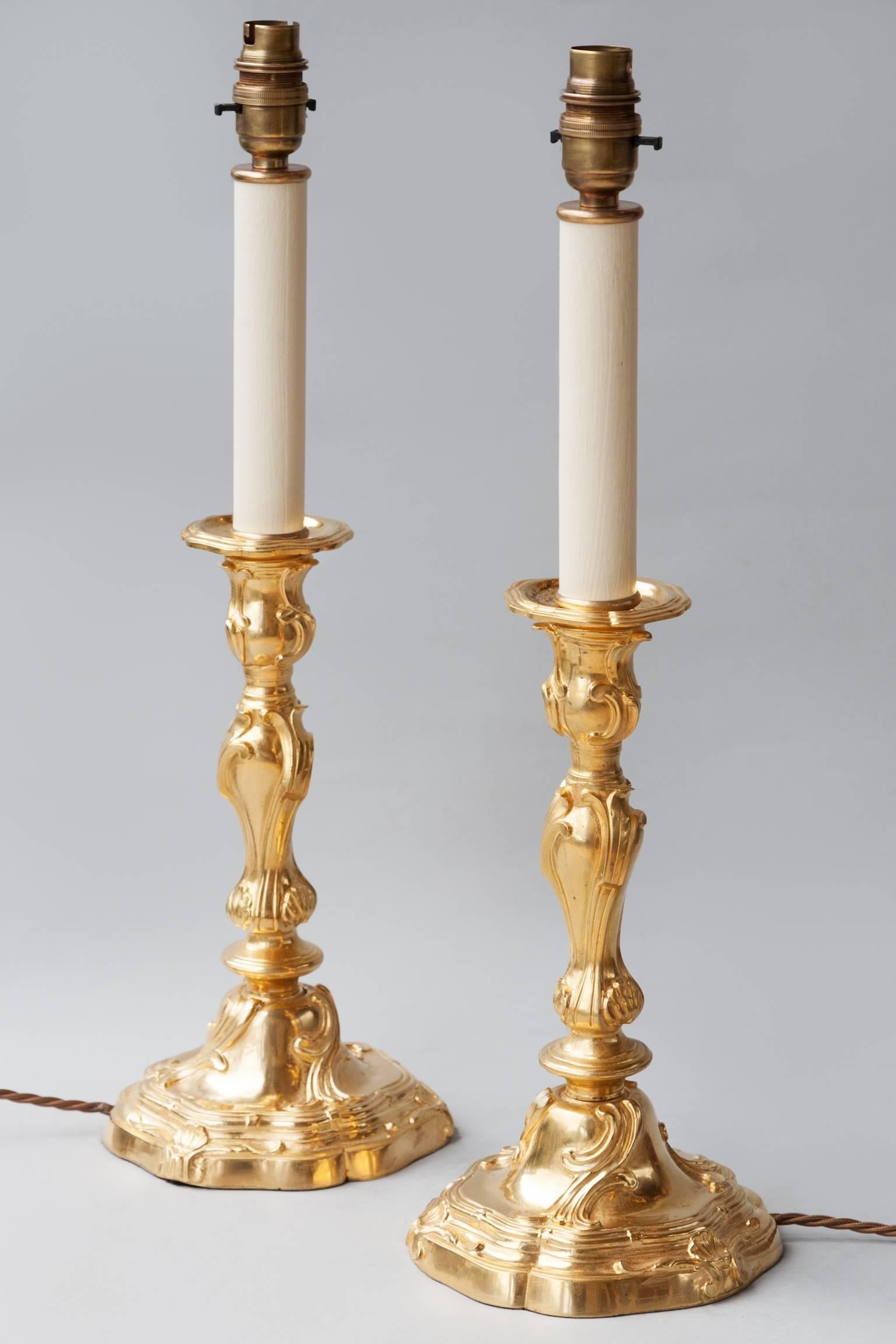 Pair of gilt bronze Louis XV style candlesticks with ornate scrolling design and shell motifs.
France, circa 1880. 
Presently converted to lamps with faux candles and electrified for the UK.
Shown here with 14