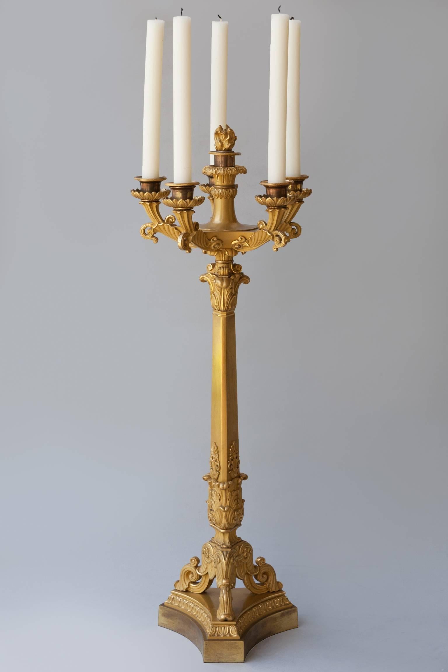 The dished top with five outscrolling arms and a central candleholder surmounted by a detachable flaming finial or flambeau.
The triangular central column on a tripod base with three scrolling feet mounted on a triangular concave base.
The whole