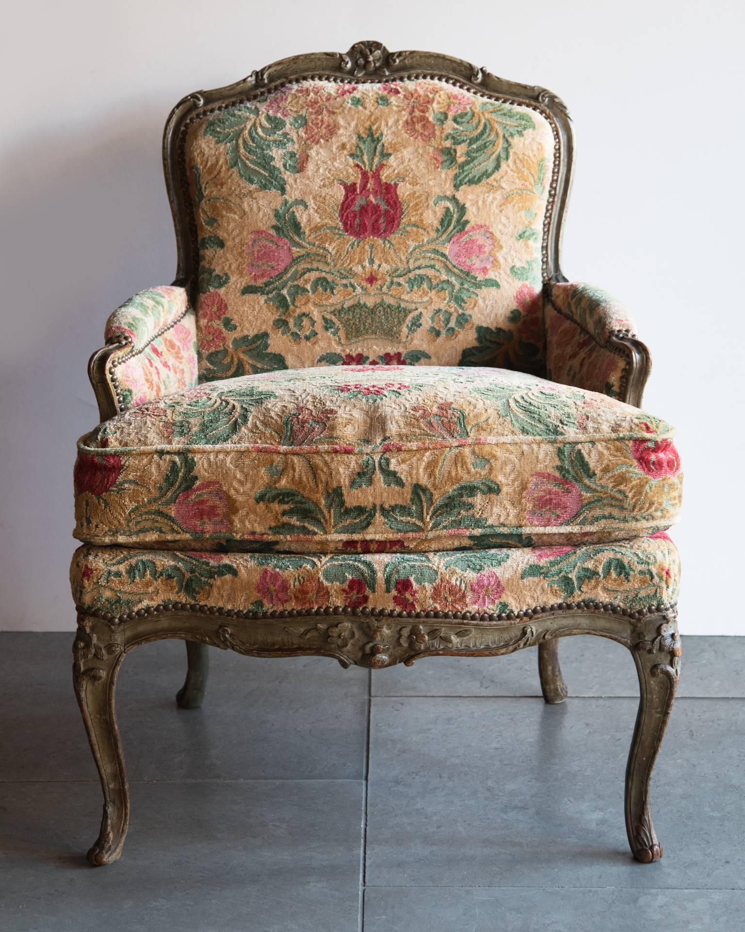 Louis XV upholstered armchair with carved arms and legs, with a central flower motif on the top and bottom aprons, curved feet terminating with carved acathus leaves. Upholstered in later polychrome fabric similar to cut velvet. Probably original