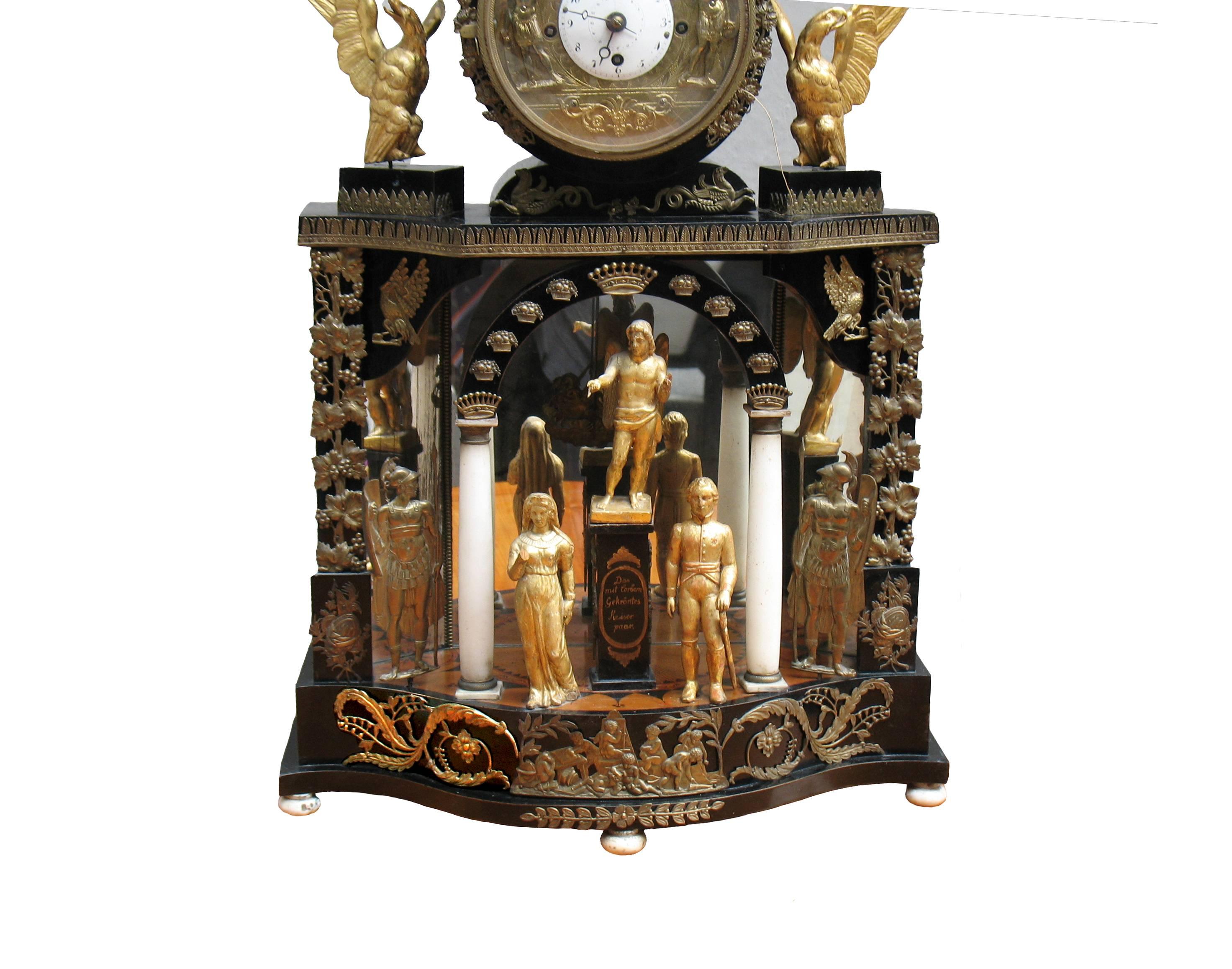 A splendid showpiece, ebonized clock case, magnificently brass-mounted (remaining all original parts), giltwood sculptures. Temple with mirrored wall, marquetry floor, stained woods, pen works, arched portal with obelisk inscribed "Das mit