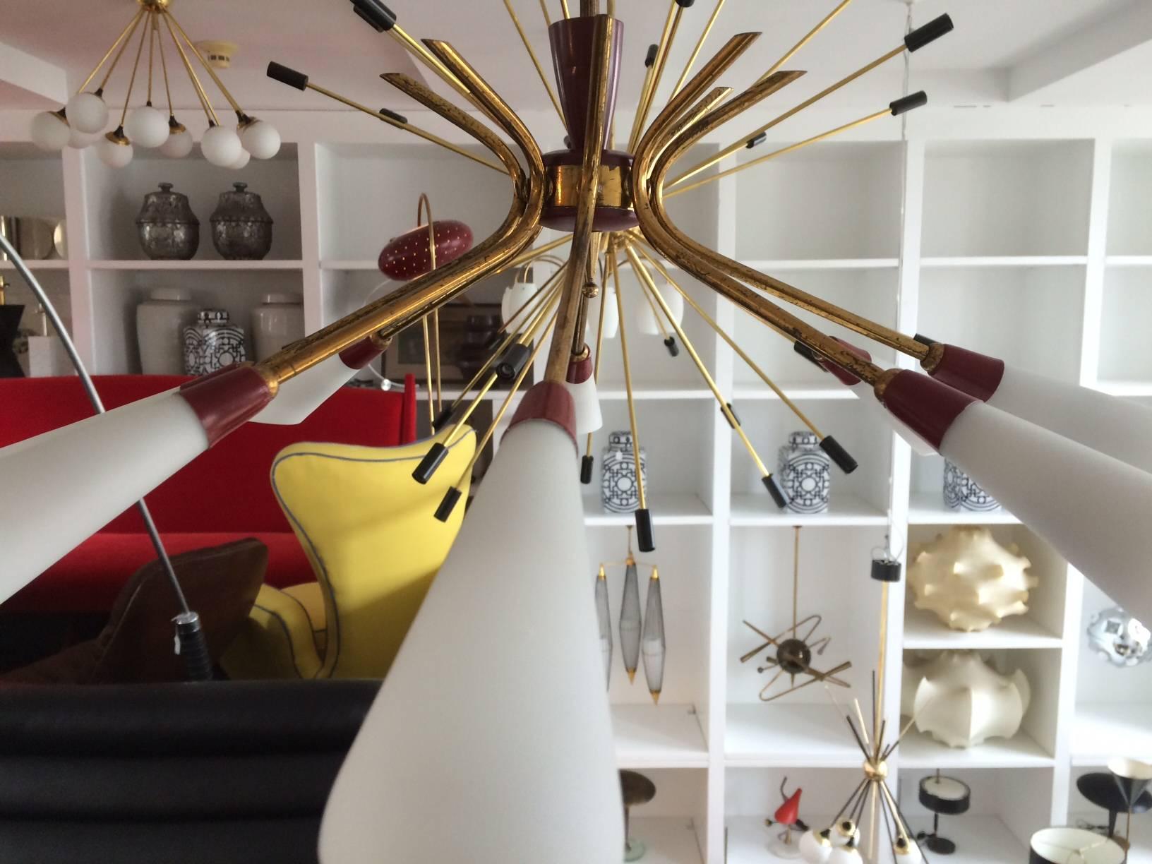 A graceful eight-arm or eight-light chandelier with brass tubular arms, distinctive red enameled details and handblown opaline glass open shades which can be directed down (as shown) or up.