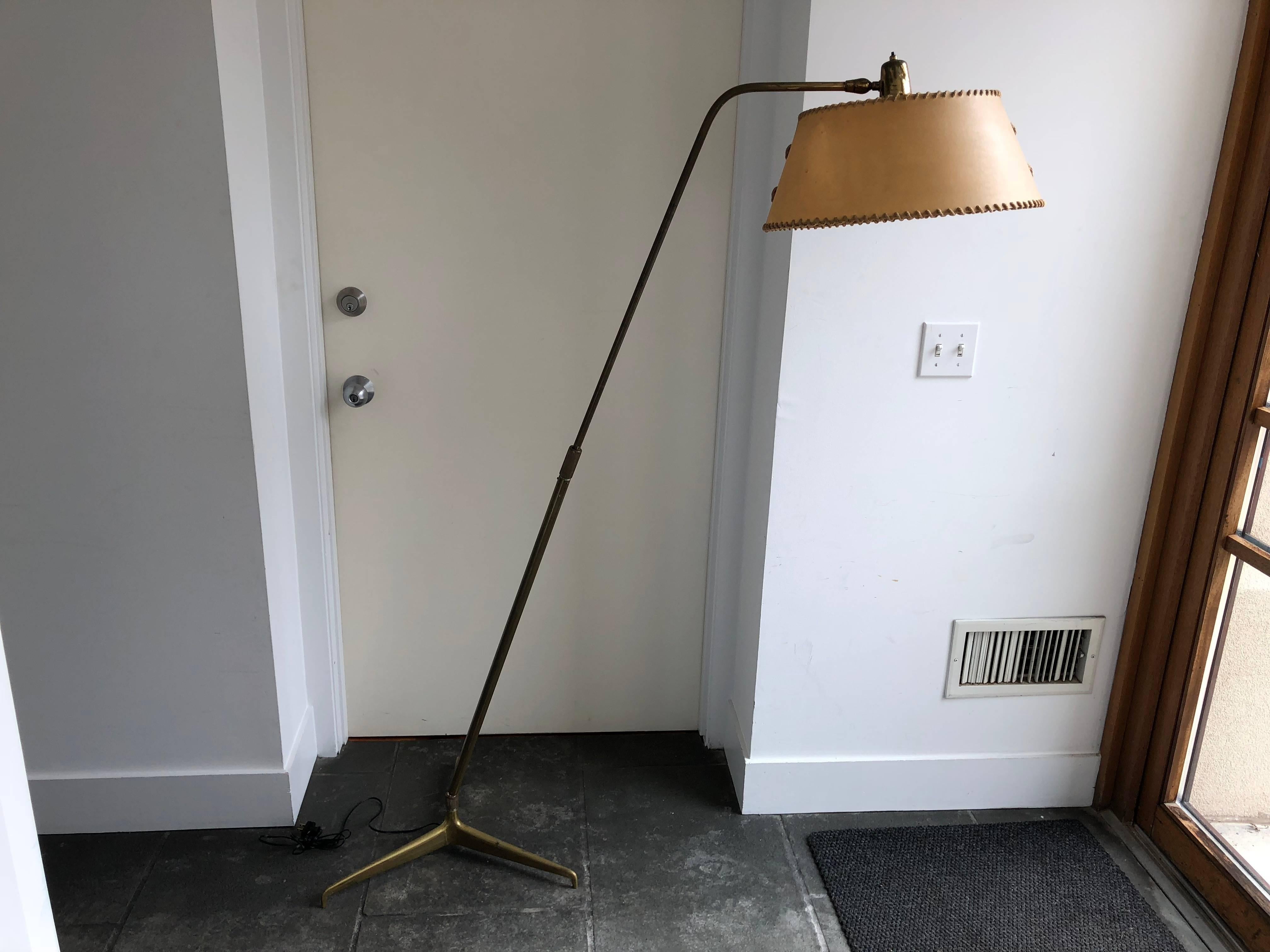 Vintage Italian brass adjustable floor lamp designed by Giuseppe Ostuni and manufactured by Oluce.  Has a brass tripod base and adjustable brass rod which holds the swivel height adjustable stem and parchment paper shade.  1950's

