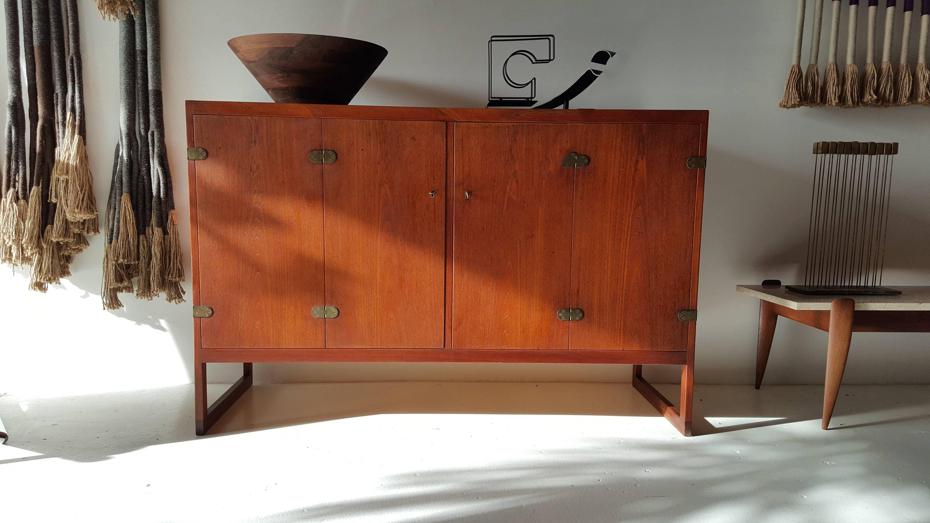 Elegantly understated Danish modern teak cabinet designed by Borge Mogensen for P. Lauritsen and Son. Two bi-fold doors open to reveal four oak finger-jointed drawers and two shelves. The exposed brass hinges on this piece add just the right touch