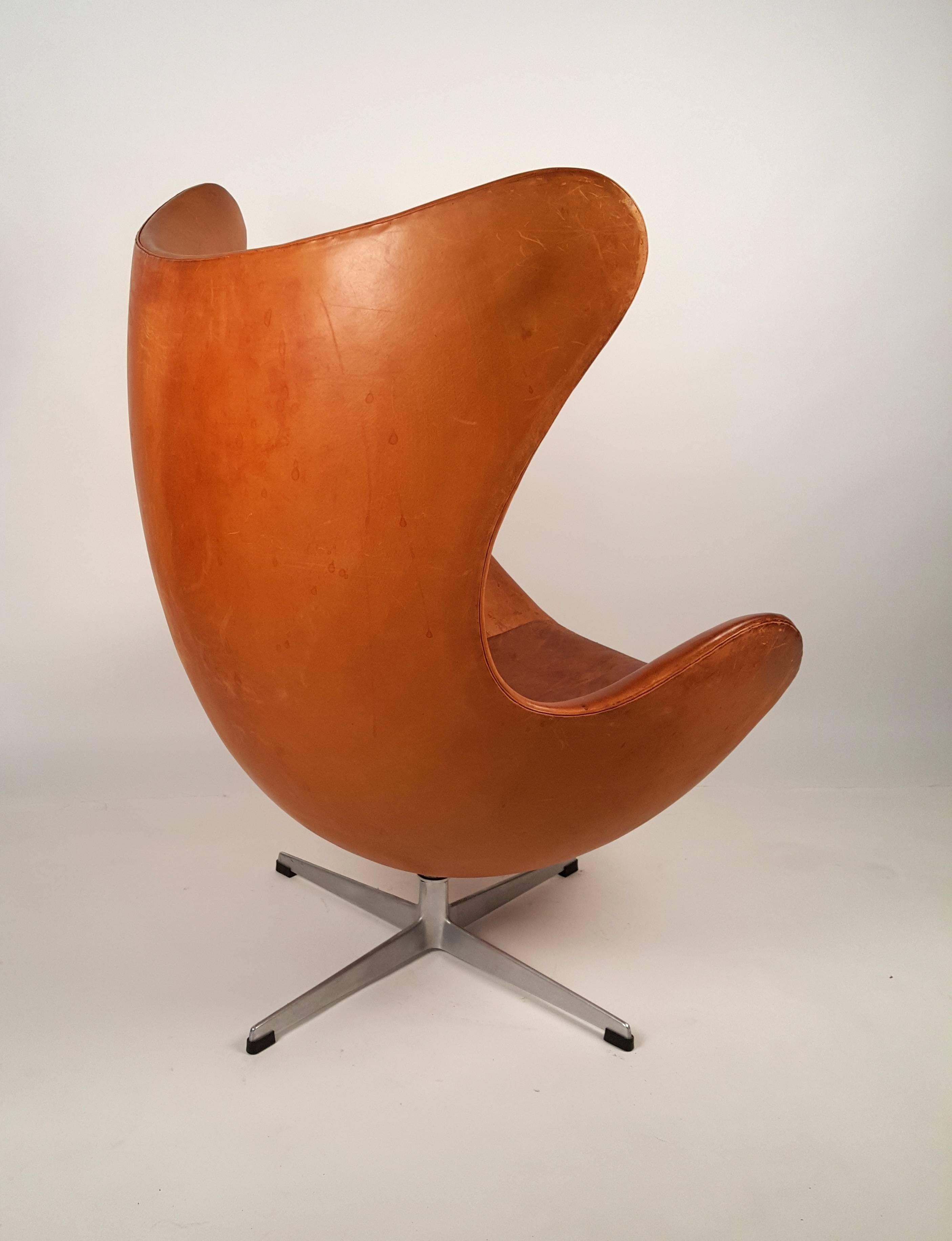 Early production Egg chair with matching ottoman in original cognac leather designed by Arne Jacobsen and produced by Fritz Hansen, Denmark. The beautiful distressed patina to the leather of this well loved chair was achieved by many years of