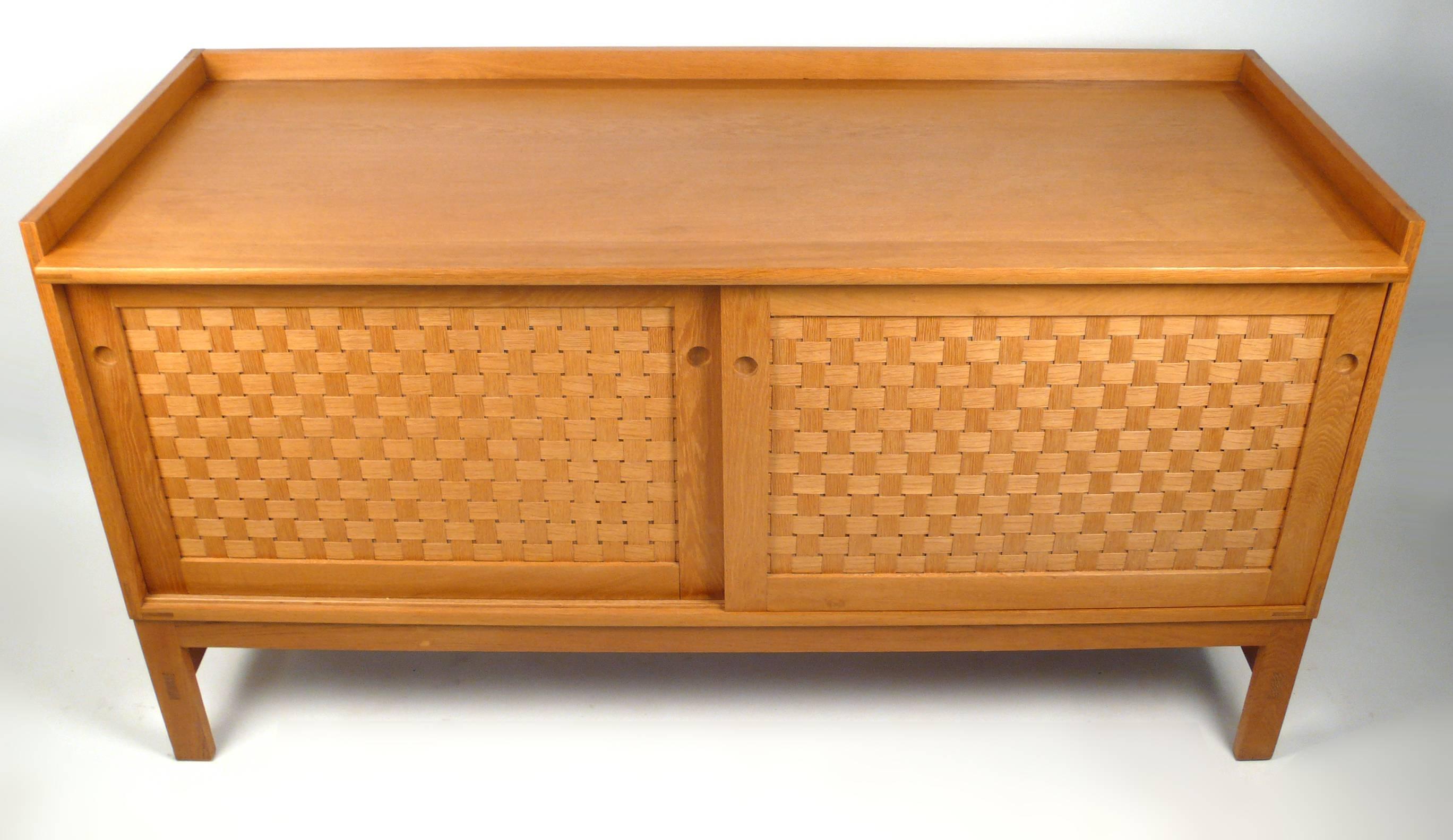 A fine and rare Danish modern oak sideboard designed by Ilse Rix for Uldum Møbelfabrik. This piece is generously proportioned and the woven front sliding doors open to reveal a series of finger jointed sliding drawers, some of which are lined in