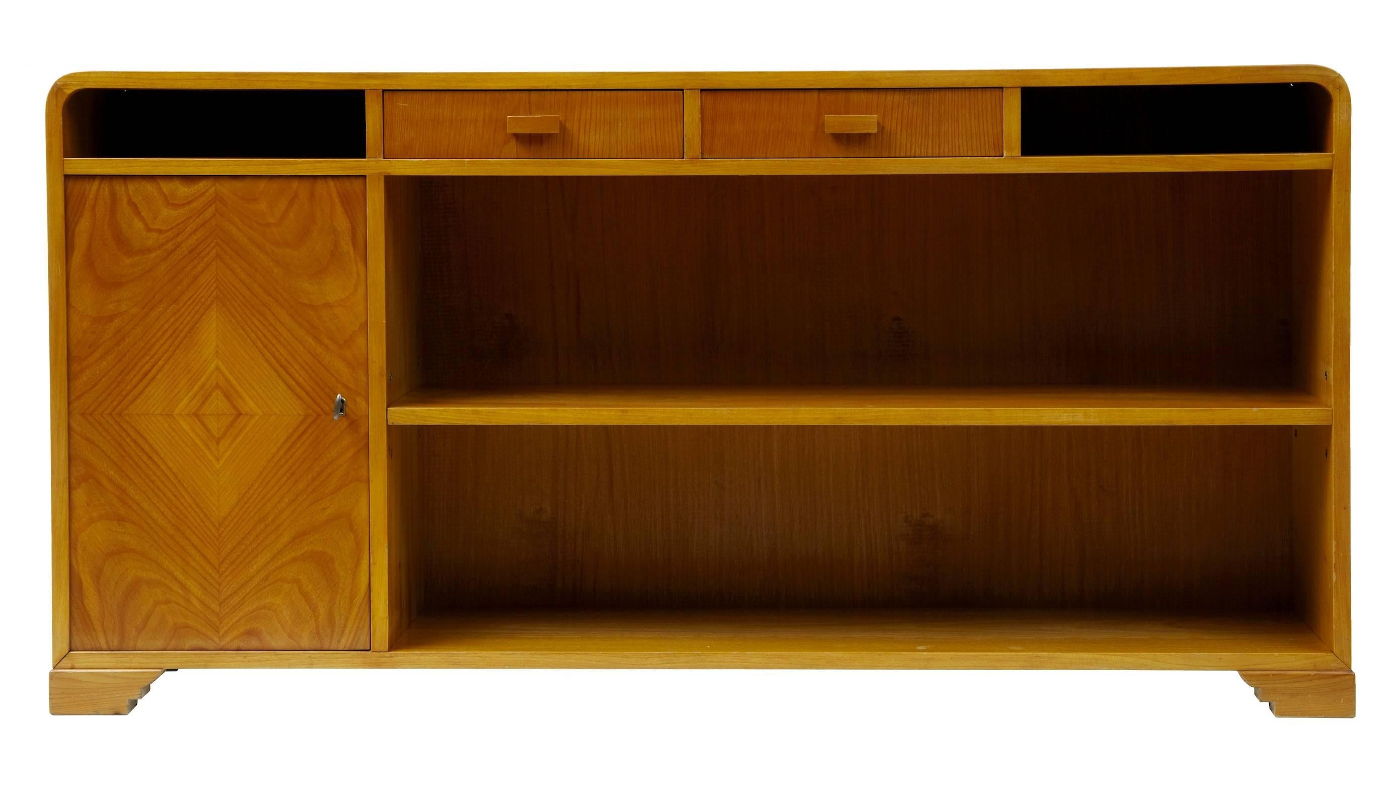 Good quality late art deco elm bookcase circa 1950
Stylish curved form top, below which are 2 open sections and 2 drawers.  Single shelf main bookcase section, which quarter veneered single door cupboard containing a further shelf.
Nice rich