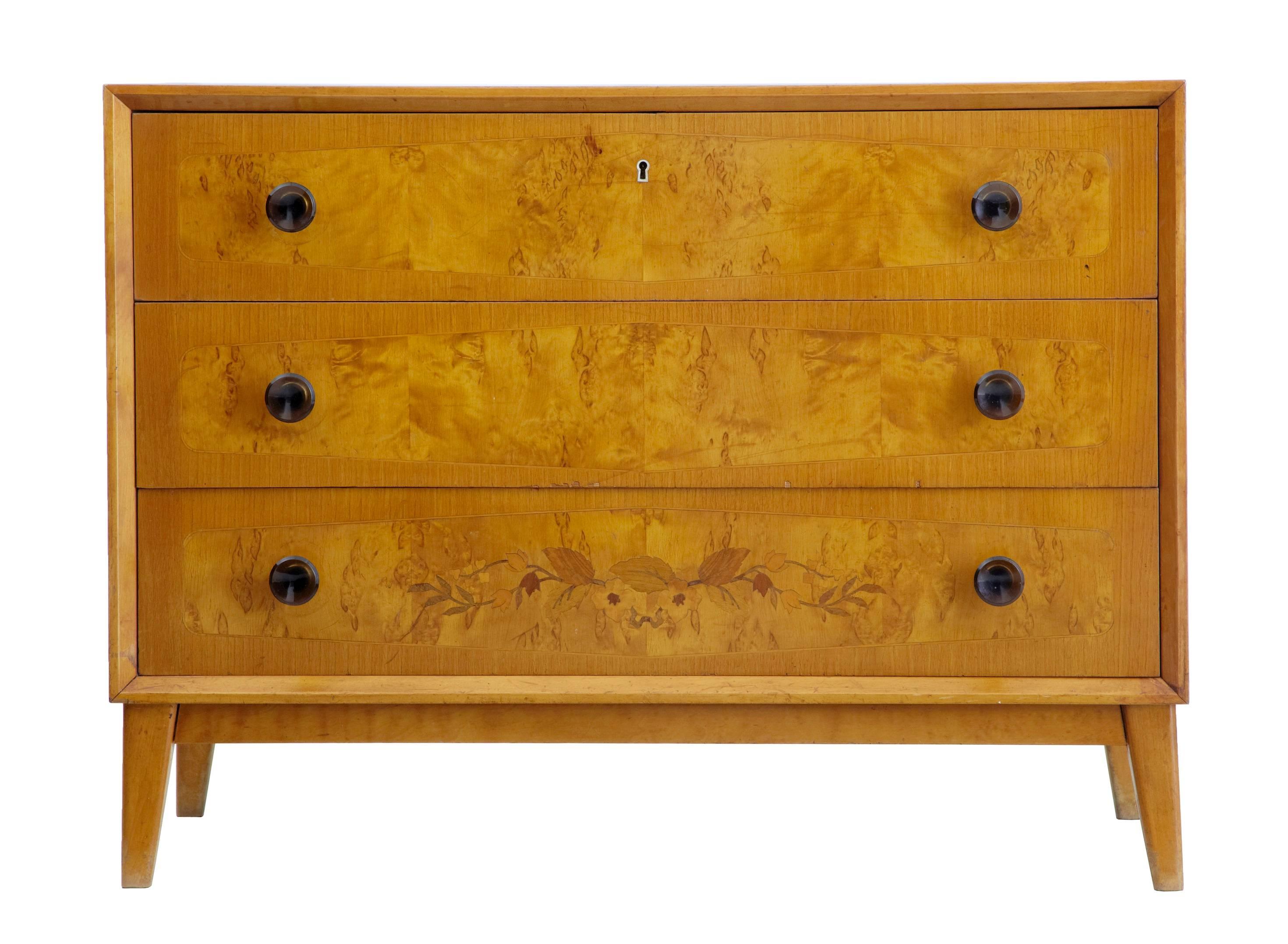 Three-drawer chest with inlaid bottom drawer, circa 1950.
Crossbanded and strung drawer fronts, with faux colored glass handles.
Standing on tapering legs.
Good color and very stylish.

Minor veneer losses to middle drawer (photographed).
No