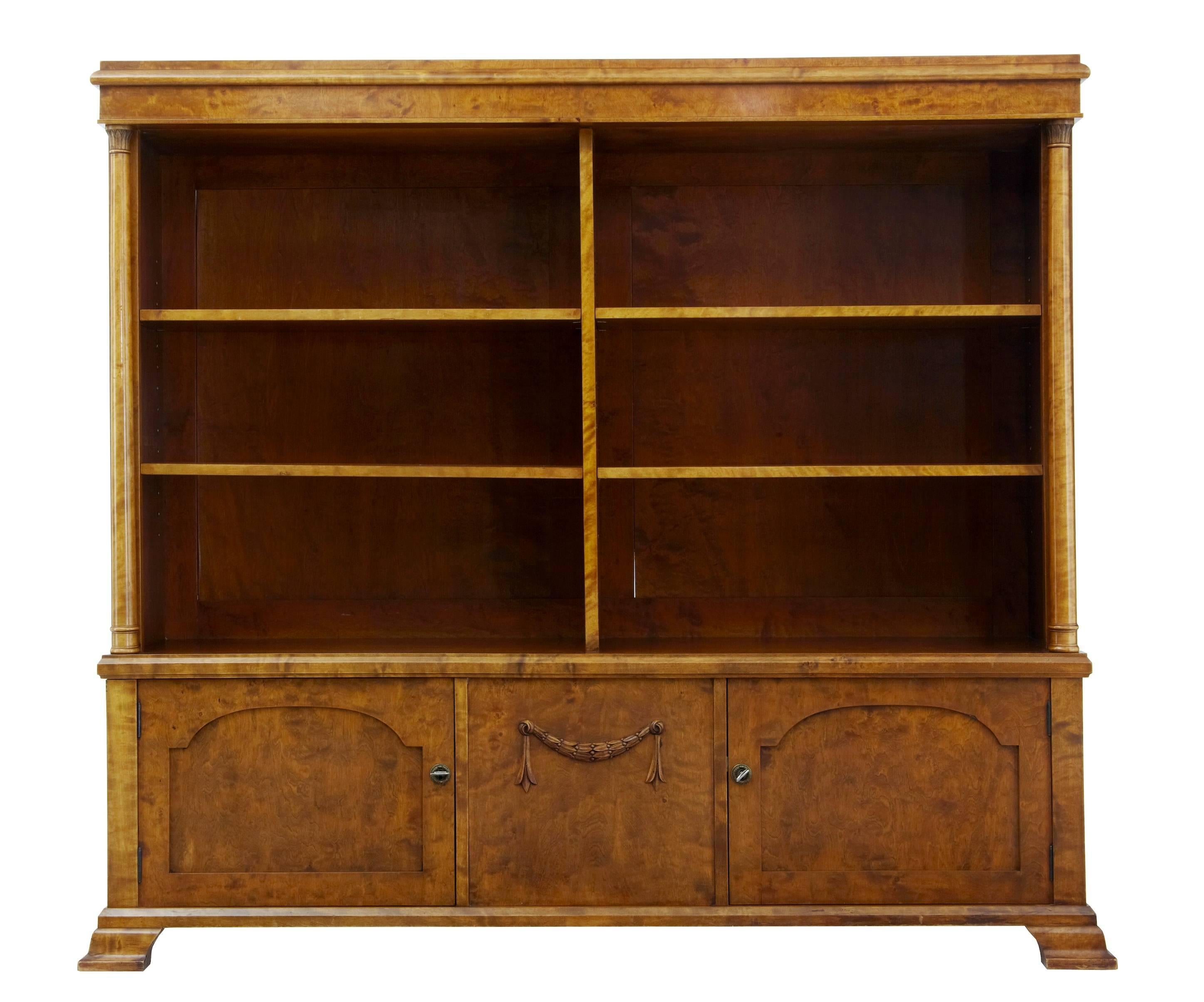 Beautiful rich birch open bookcase, circa 1910.
Four adjustable shelves with a central partition, below a central panel with carved applied swag, flanked either side a single door cupboard.
Column detail runs up both front sides.

Height: 54