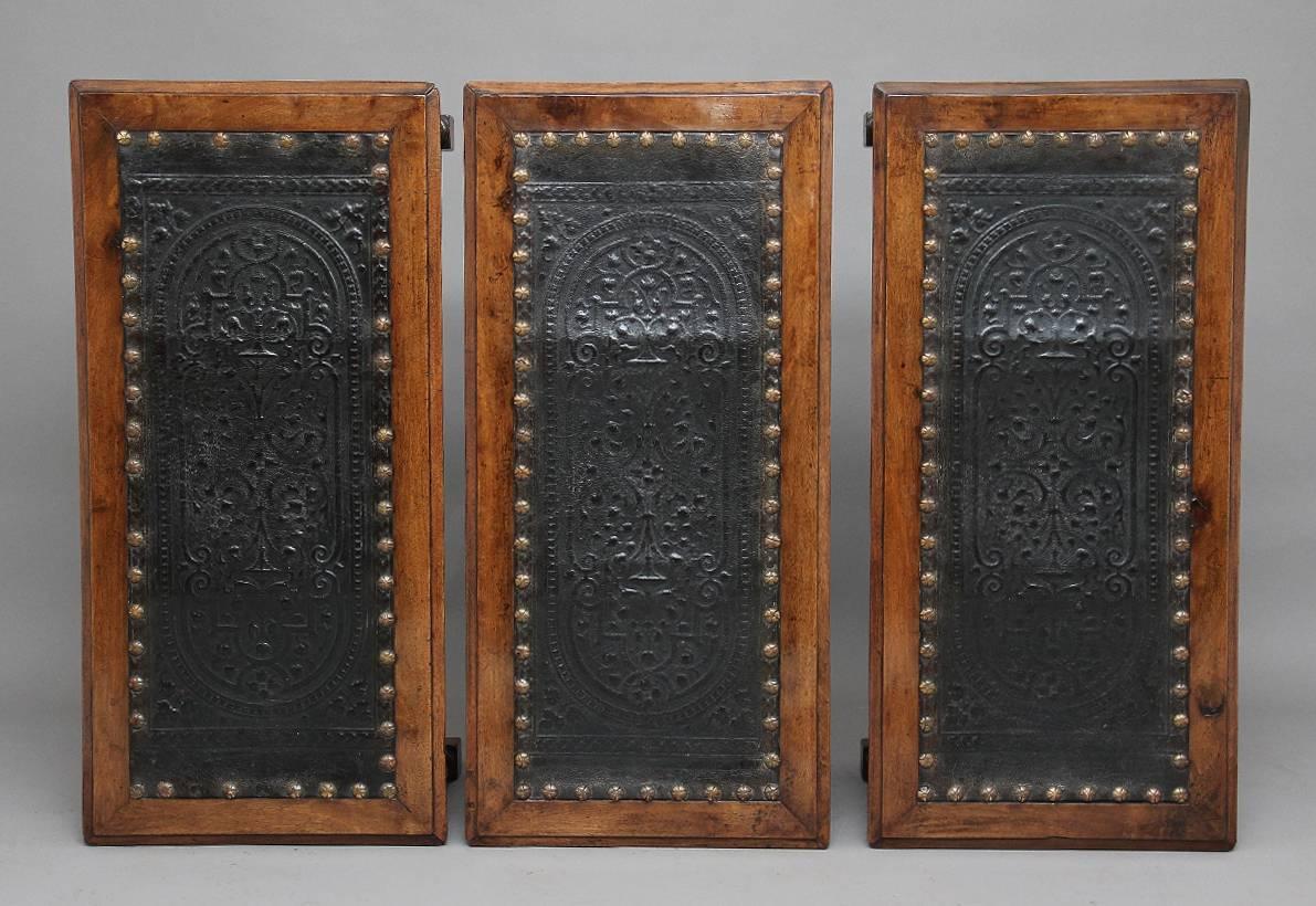 A set of three Italian walnut stools with leather tops, the leather decorated with brass studs around the edge and a pattern inscribed at the center, with a nicely shaped apron running around all sides decorated with patraes, with four carved turned