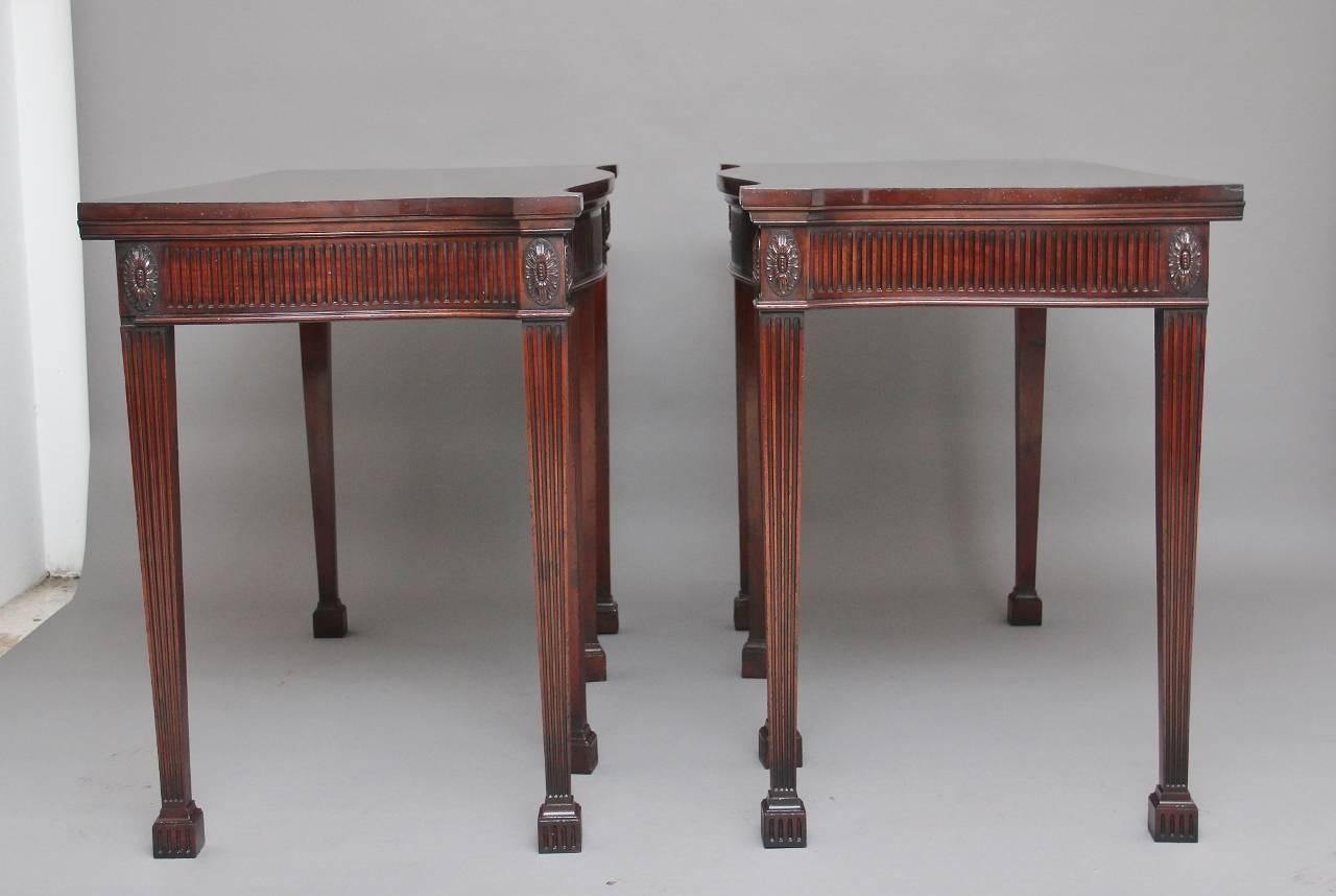 A fine pair of early 20th century mahogany console / serving tables in the Adams style, with a shaped top and a fluted apron along the front and sides decorated with carved patraes, supported on six square tapering fluted legs terminating on fluted