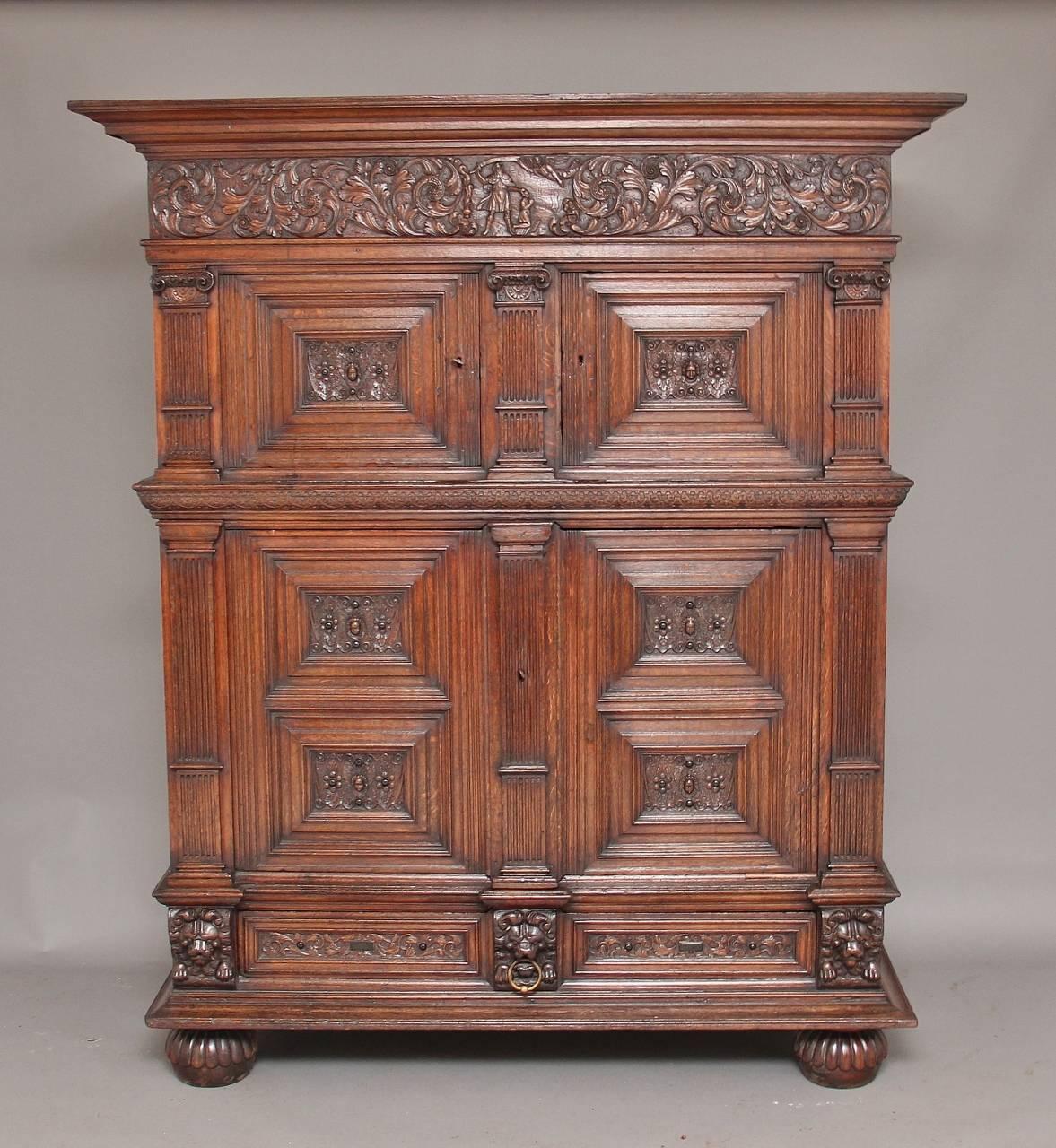 17th century Flemish oak cupboard, with two small doors above two large doors with a single drawer below, the top having a deep ogee moulded cornice with a frieze below which is finely and profusely carved, the panelled front carved with cherub