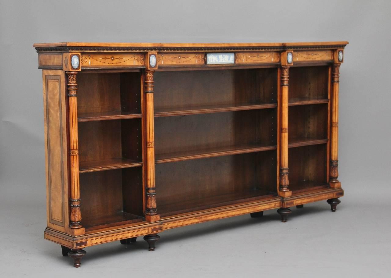 A fine quality Regency satinwood open bookcase profusely inlaid with partridgewood, the breakfront rectangular top decorated with various inlay with a anthemion inlaid frieze below which includes mother-of-pearl, and decorated with Wedgwood-style