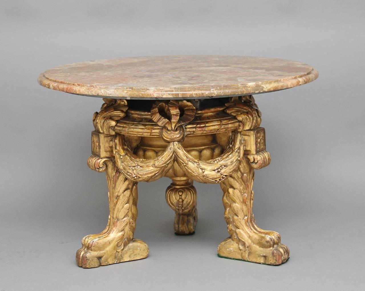 Mid-20th century Italian occasional or coffee table with a veined marble top with a moulded edge, the base made from giltwood which is heavily carved, decorated with swags which are united with the legs, standing on lion feet, circa