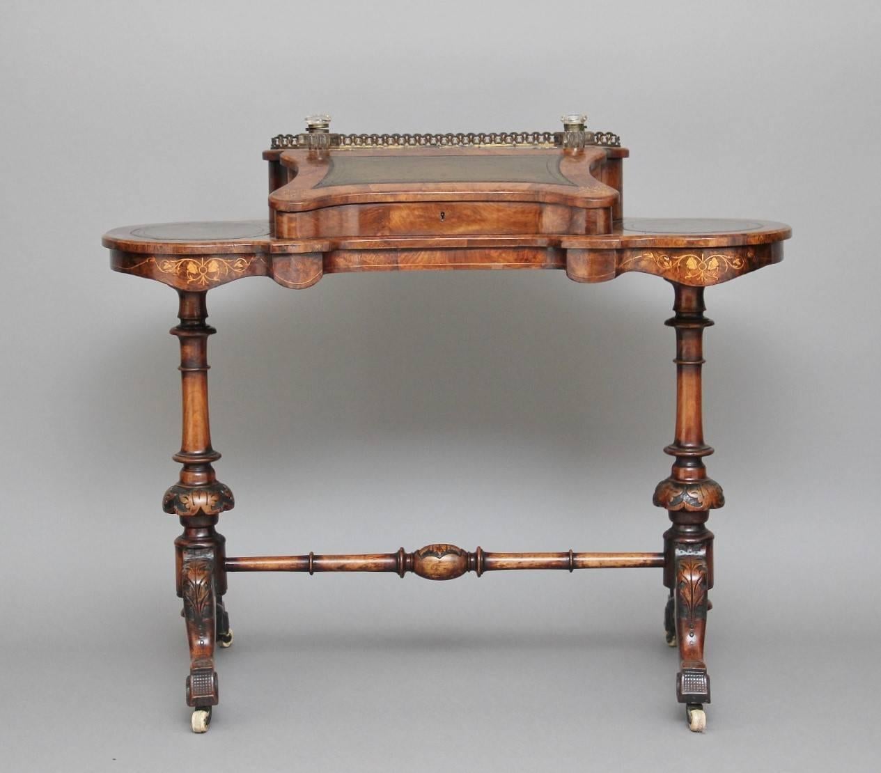 A lovely quality 19th century inlaid walnut ladies writing table, the kidney shaped top with rear brass gallery and a green leather inset slope opening to reveal a fitted interior, with a rear pen tray, flanked by glass inkwells raised on carved