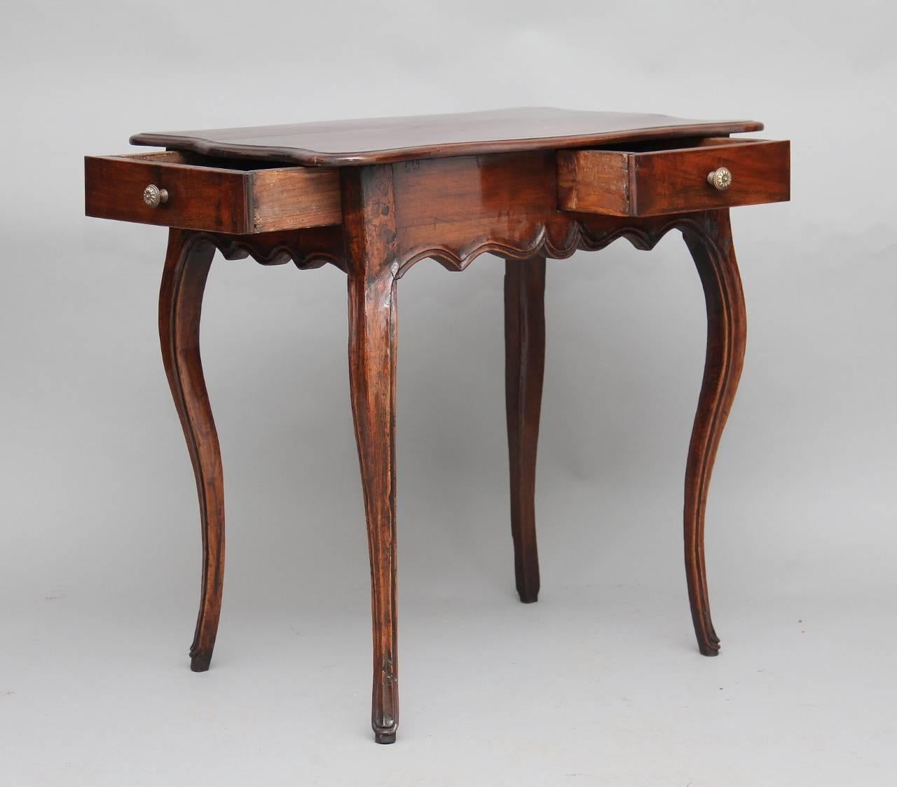 18th century French provincial side table made from fruitwood, with a nicely shaped top with a moulded edge, with two drawers below, one on the side and one at the front, with a shaped frieze running along the front, sides and back, standing on