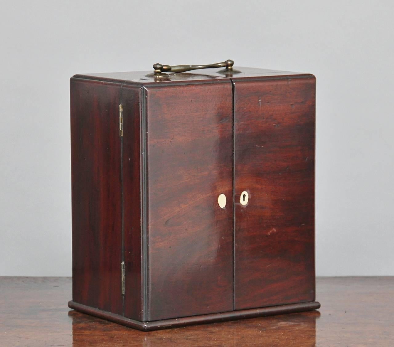 19th century mahogany apothecary cabinet, the top having a brass swan neck carrying handle, the two hinged doors opening to reveal six original glass jars above three small over two long graduated drawers which includes various medical