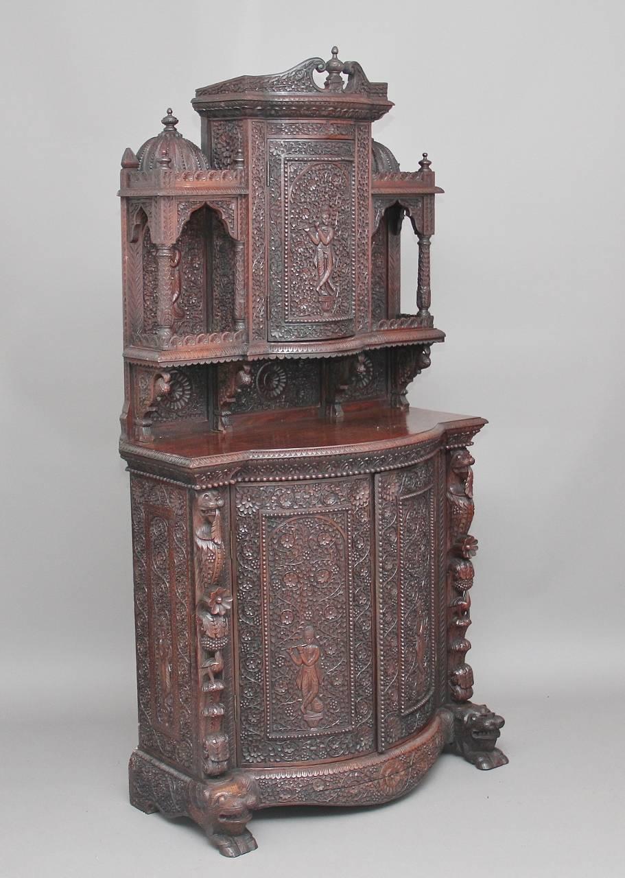 A fabulous quality 19th century Indian rosewood suite comprising of

A rosewood bowfronted cabinet profusely carved all-over, the top superstructure with one bowfronted door in the center flanked by openings topped with carved domes and finials,
