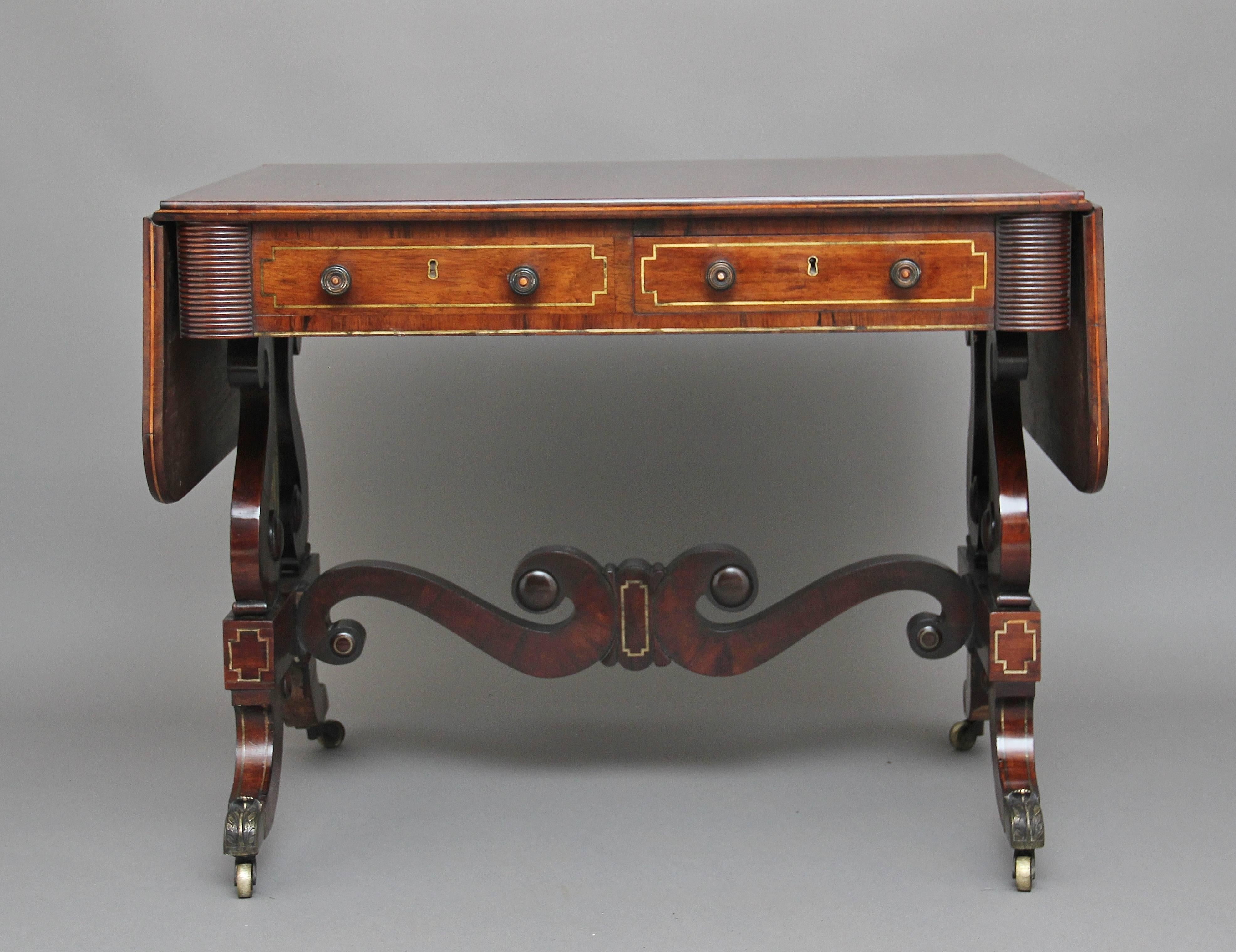 19th century rosewood and brass inlaid sofa table with a rectangular crossbanded top with drop flap sides, below the frieze consisting of two mahogany lined drawers and two false drawers, with lyre end supports raised on acanthus leaf caps and