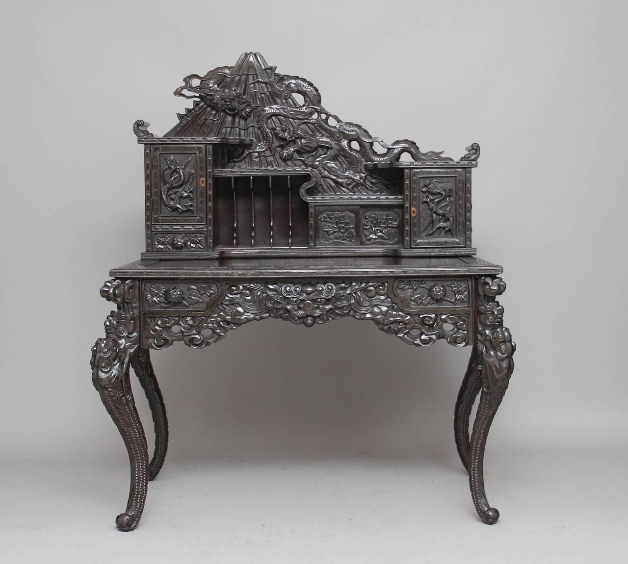 Early 20th century highly carved Chinese desk, the top section with a shaped back carved in relief with two dragons on a mountain, below with various compartments flanked either side with carved panelled doors and a small drawer on the left hand