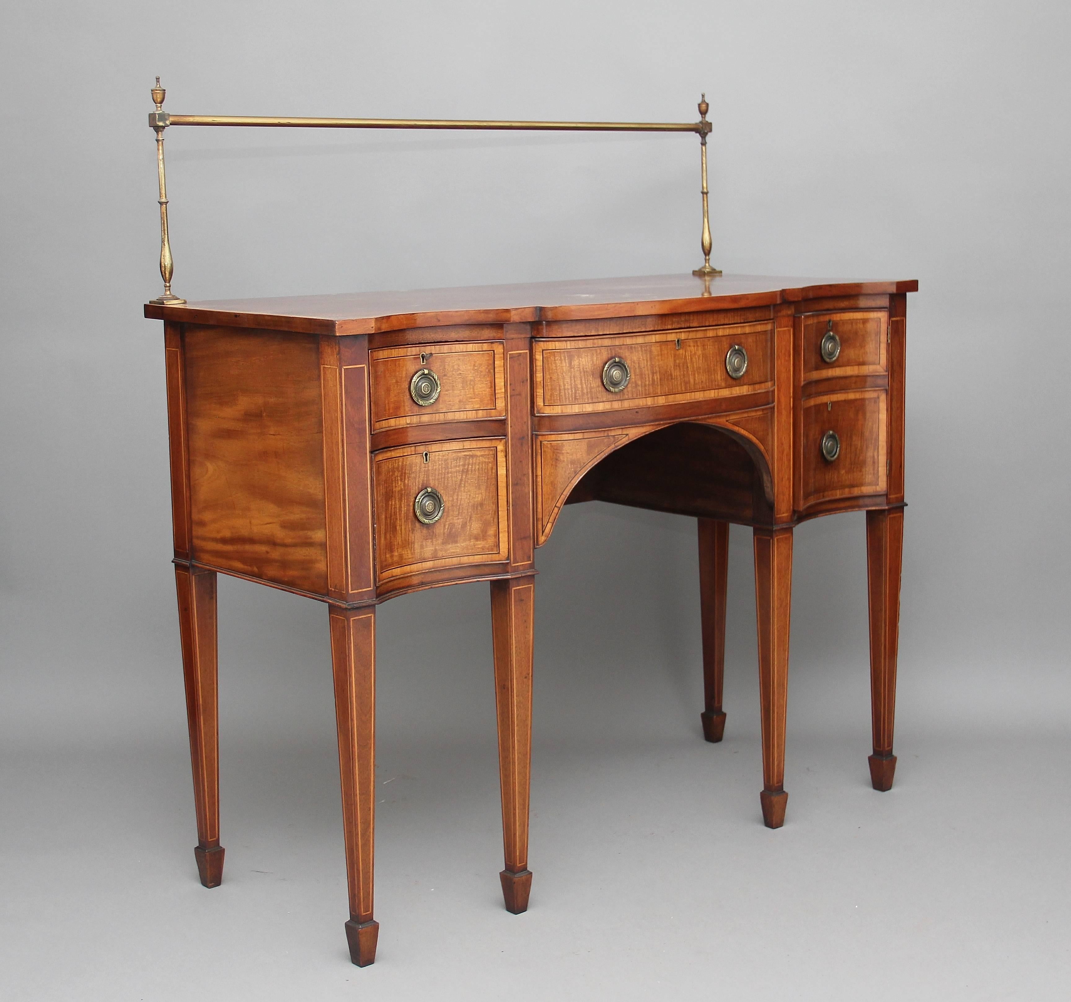 Early 20th century mahogany serpentine sideboard with a nice shaped top with satinwood crossbanding, the back of the top having a brass gallery, the sideboard having a single central drawer with two graduated drawers to the left and a cupboard to