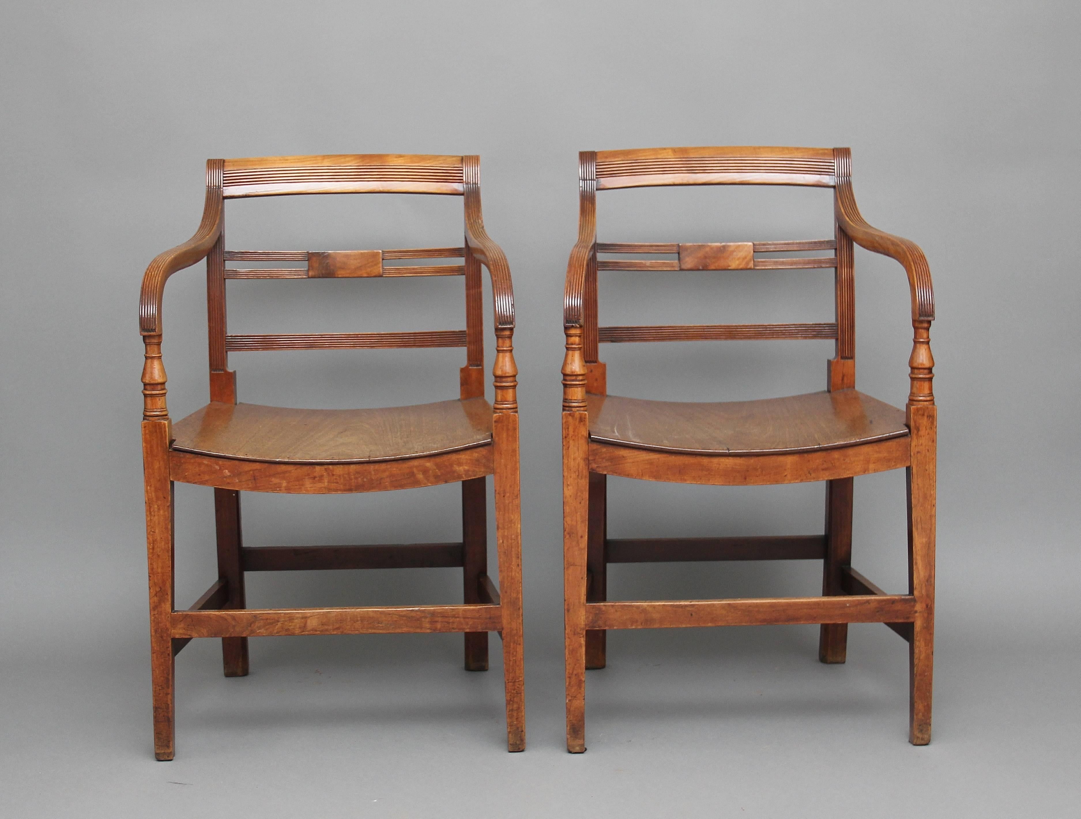 A pair of early 19th century fruitwood country open armchairs with a slightly arched hardwood seat, with three reeded back rails, shaped reeded arms with nice turned supports, on square legs supported with front, side and back stretchers, circa