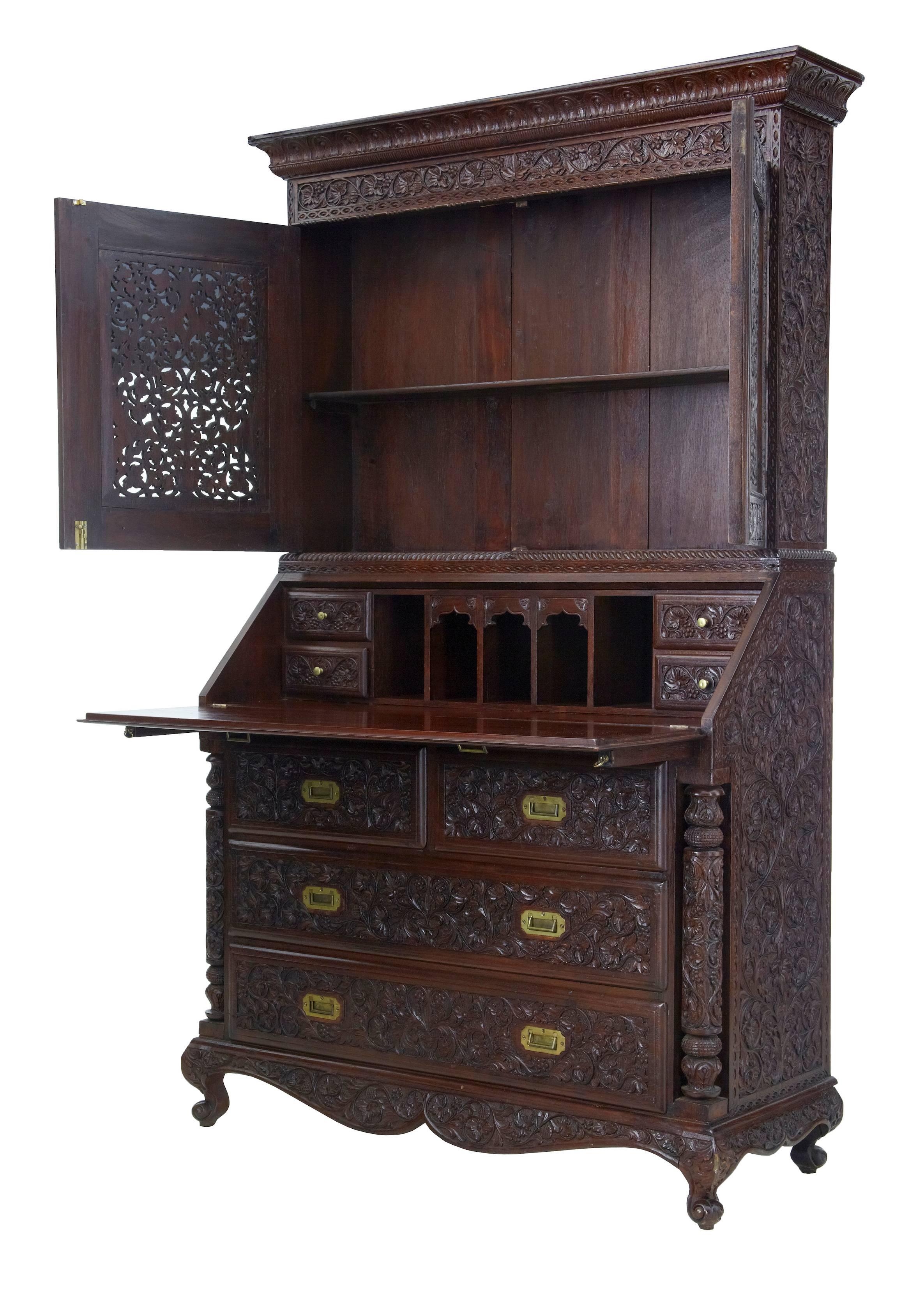 Fine quality Anglo-Indian bureau bookcase, circa 1895.
Profusely carved all-over in padouk.
Two parts, top section of a pierced double door cupboard that opens to reveal a narrow shelf.
Bureau fall opens to a fitted interior of four drawers and