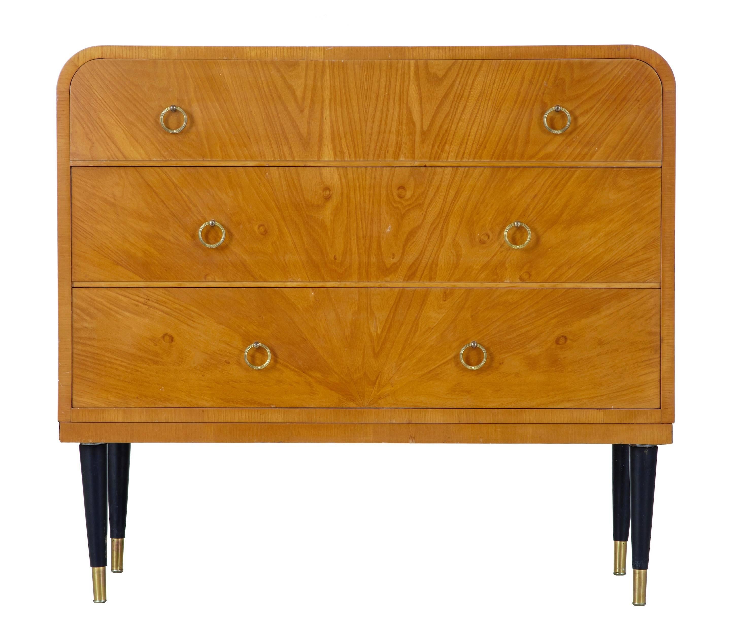 Swedish elm chest of drawers in the deco taste, circa 1950.
Three drawers with brass ringed handles.
Shaped sides, standing on ebonised legs with brass tips.

Some polish loss to the top, please see pictures. We could undertake the work at