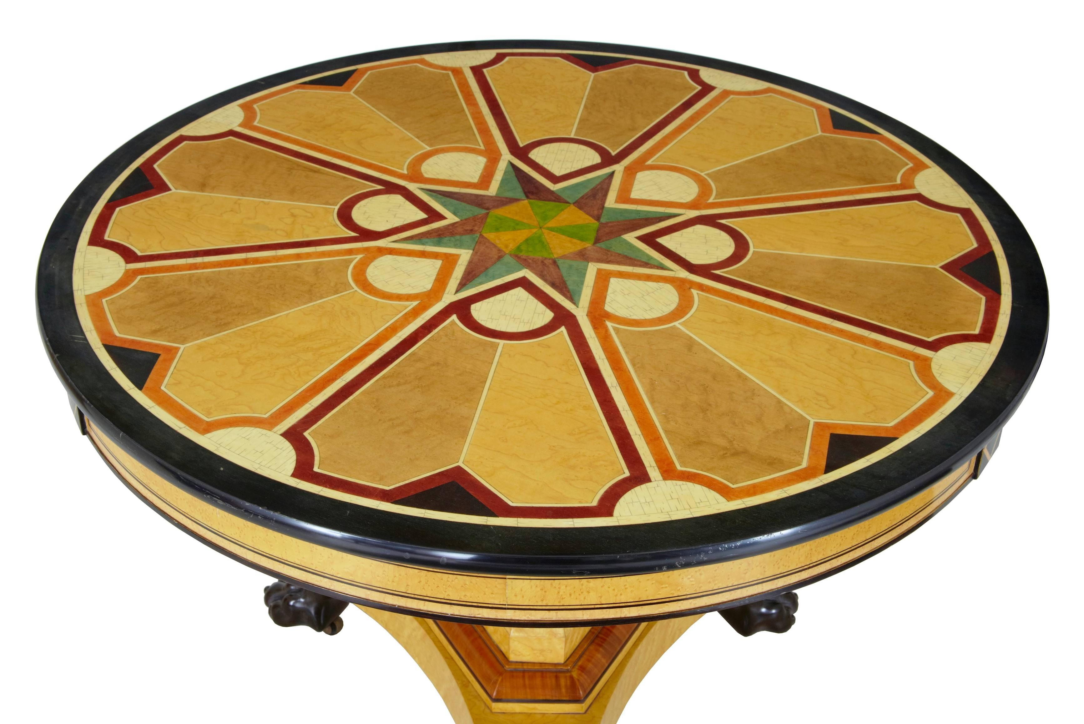 Good quality decorative table, circa 1970.
Laminated inlaid top, simulating various inlays and veneers, supported on a birch triform base and standing on ebonised lion paw feet.

Measures: Height: 30 1/4