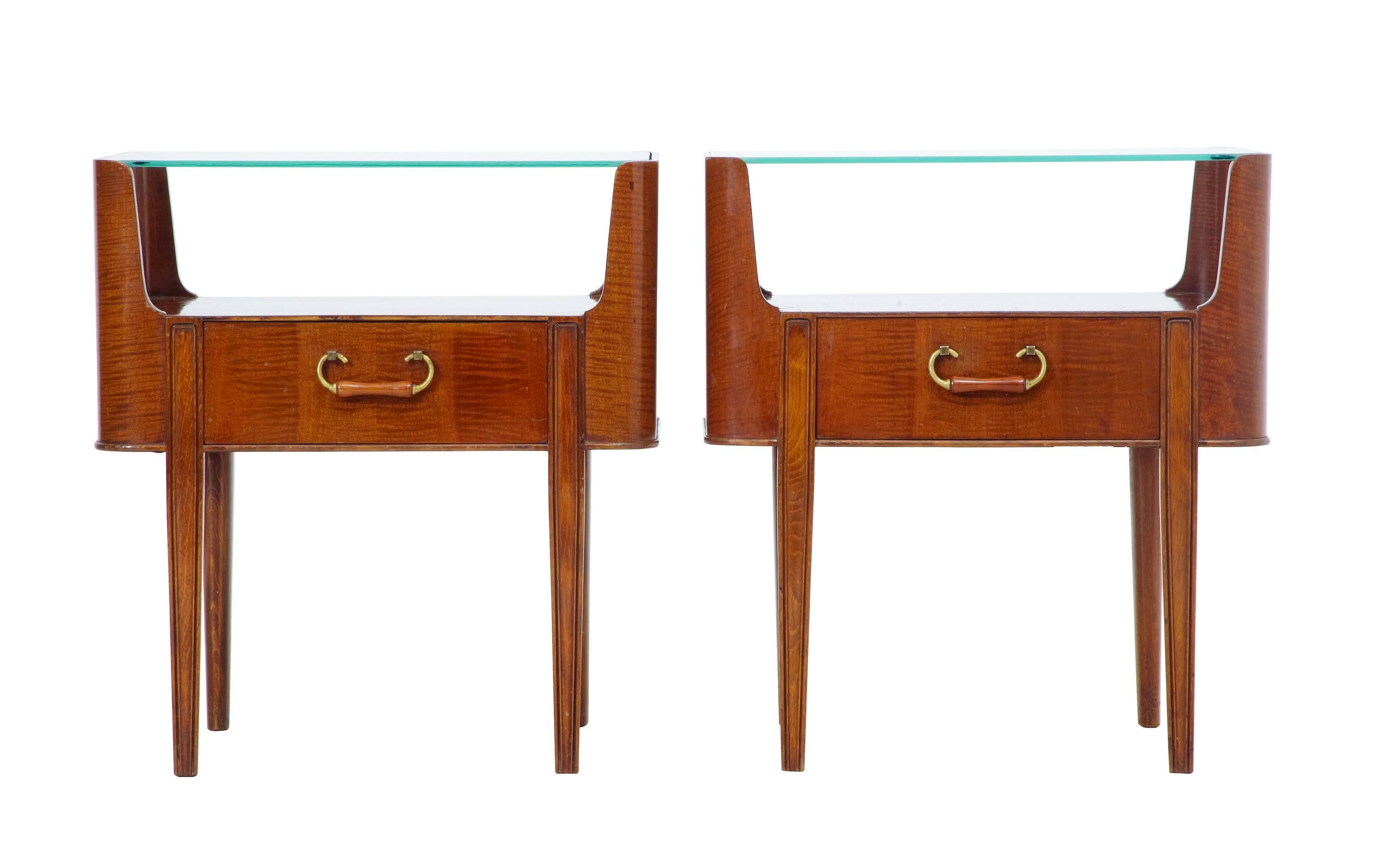 Pair of Art Deco inspired Scandinavian bedside tables, circa 1960.
Each with drop in glass top.
Open aperture for storage, below which a single drawer with brass and wood handle.
Standing on turned legs.
Some surface marks and evidence of normal