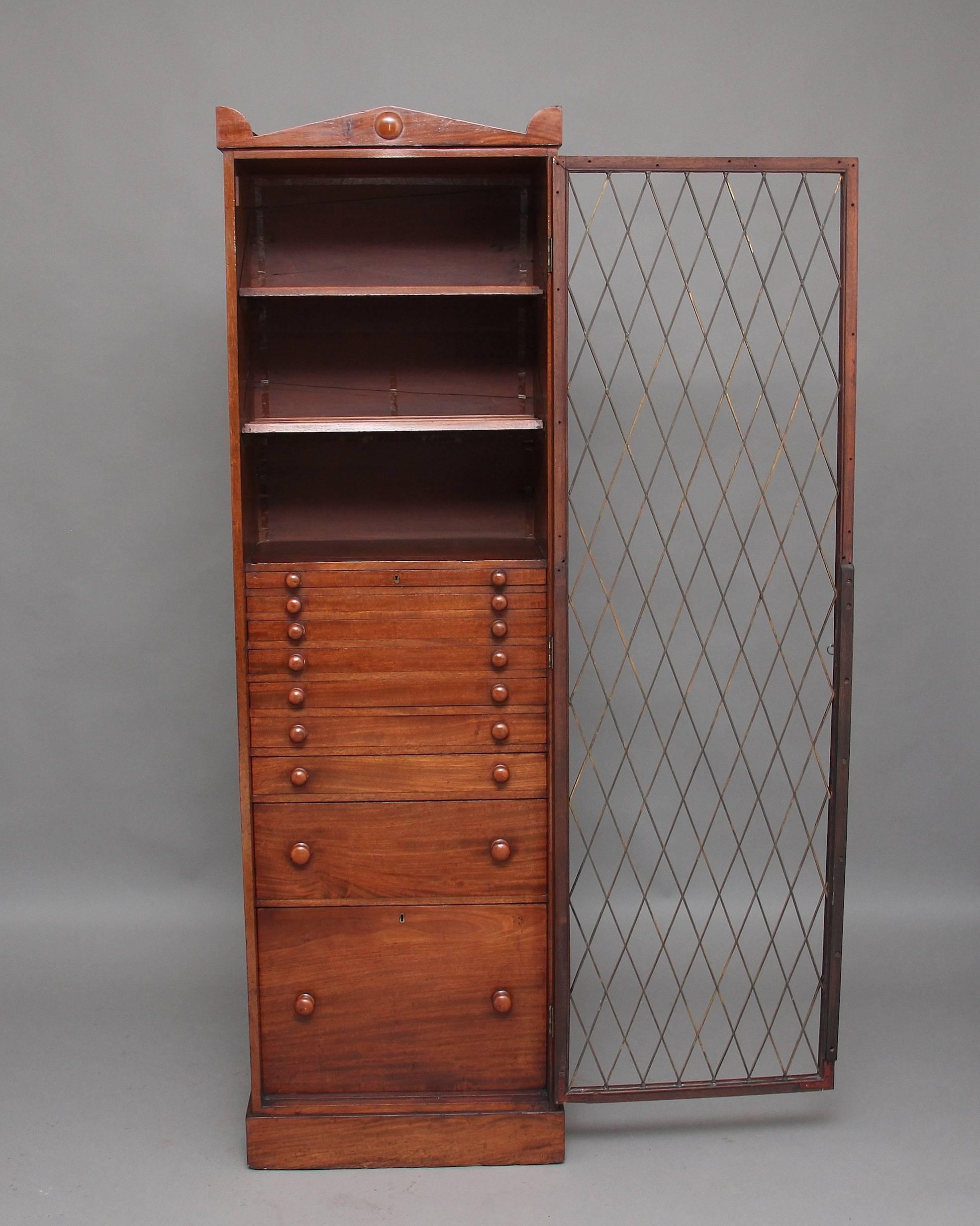 19th century mahogany collectors cabinet, the top having an architectural pediment, the single grill door with original lock and key opening to reveal two shelves at the top and nine graduated drawers below with original mahogany turned knobs, two