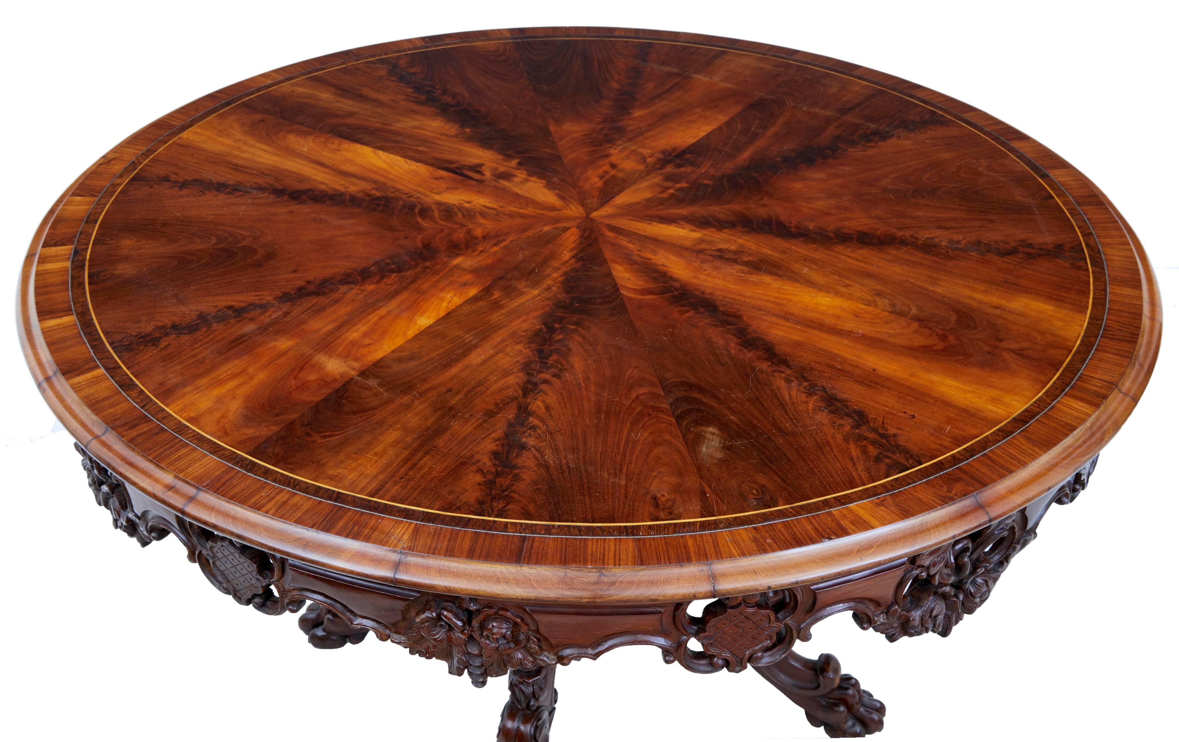 Good quality Danish centre table, circa 1860.
Flame mahogany top with boxwood stringing and pewter line, crossbanded with rosewood. Pierced carved apron.
Standing on a profusely carved base of four scrolling legs which surround a large central