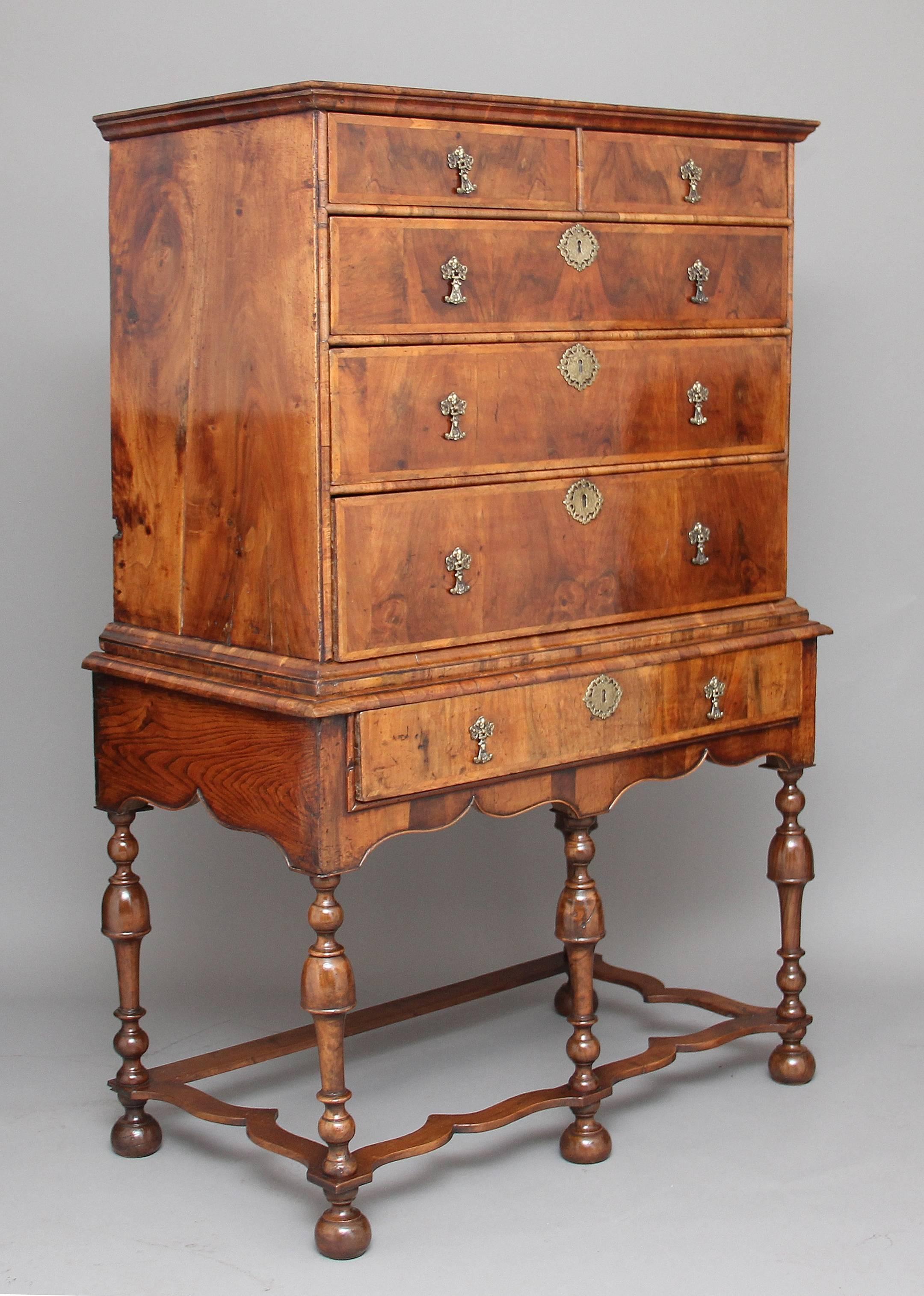 Early 18th century walnut and herring bone banded chest on stand, the chest having a stepped moulded cornice above a combination of two over four graduated long elm lined drawers, including a single drawer to the stand, with foliate embossed brass