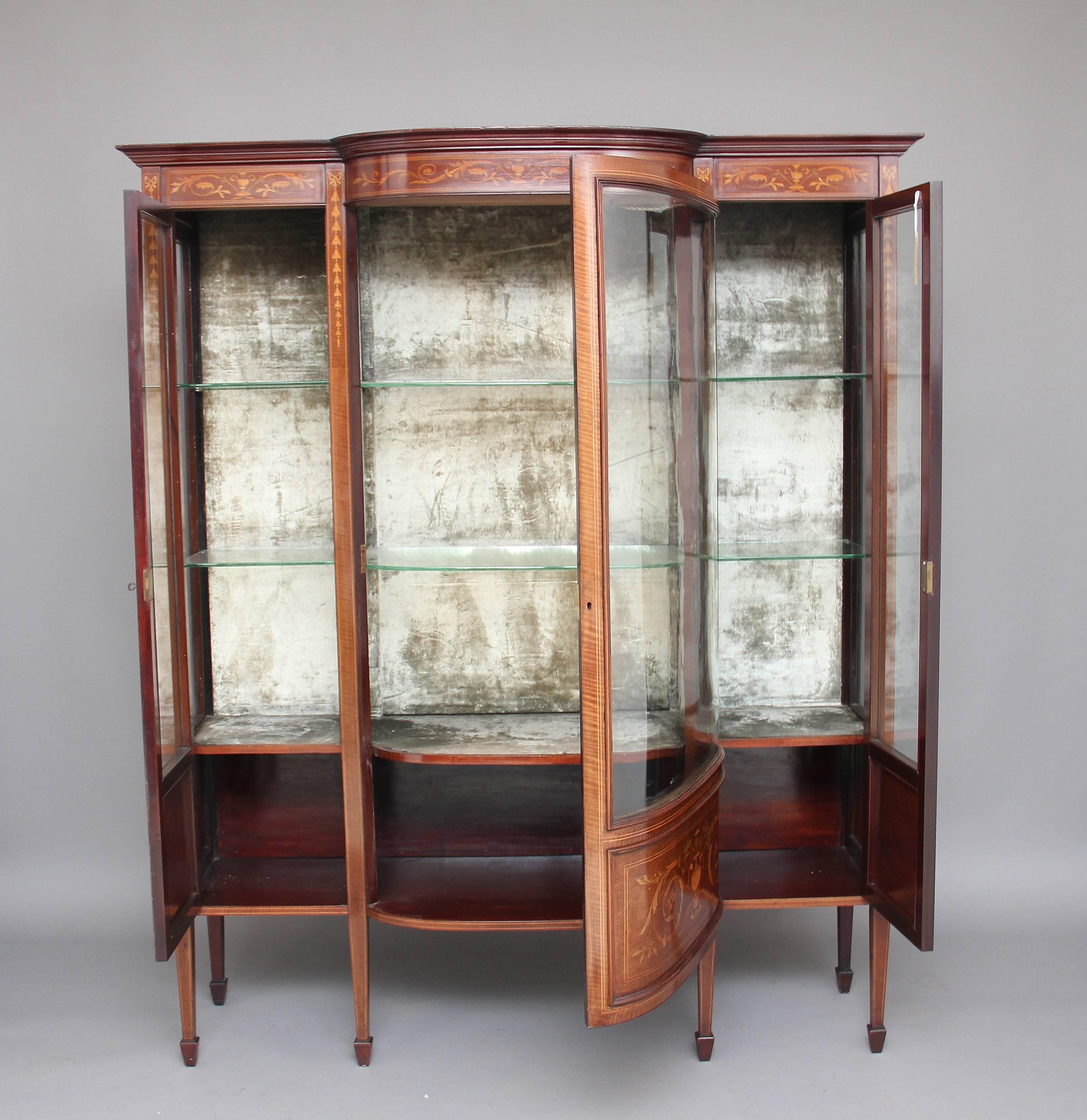 Early 20th century mahogany and inlaid display cabinet, the stepped moulded cornice above an inlaid frieze, with three glazed doors below, the middle bow fronted glazed door flanked either side by single glazed doors, each door opening to reveal two