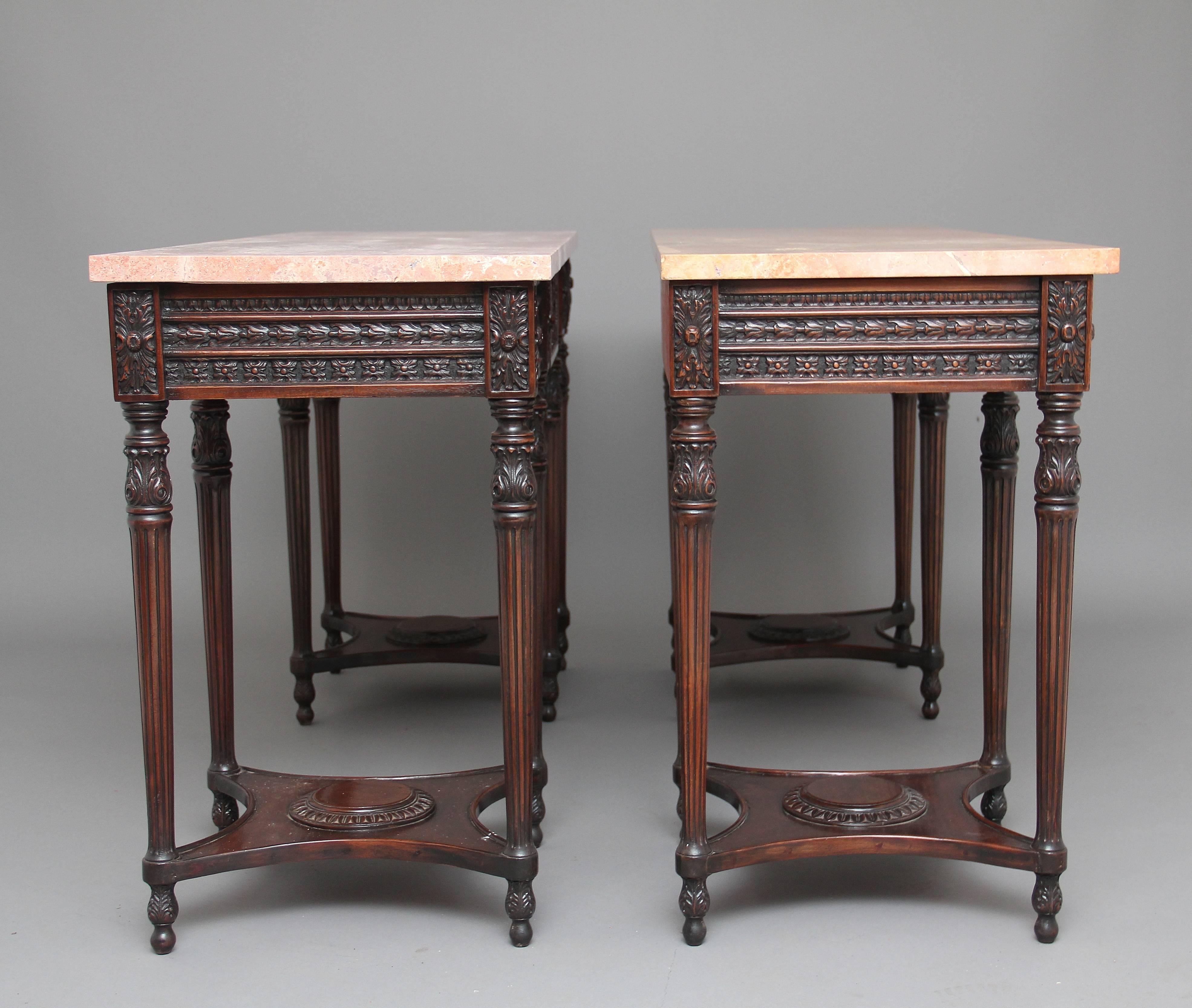 A pair of early 20th century mahogany and marble-top console tables in the Adams style, the console’s having pink flecked marble tops, with a profusely carved frieze below with carved patraes and a single drawer at the centre, the frieze also having