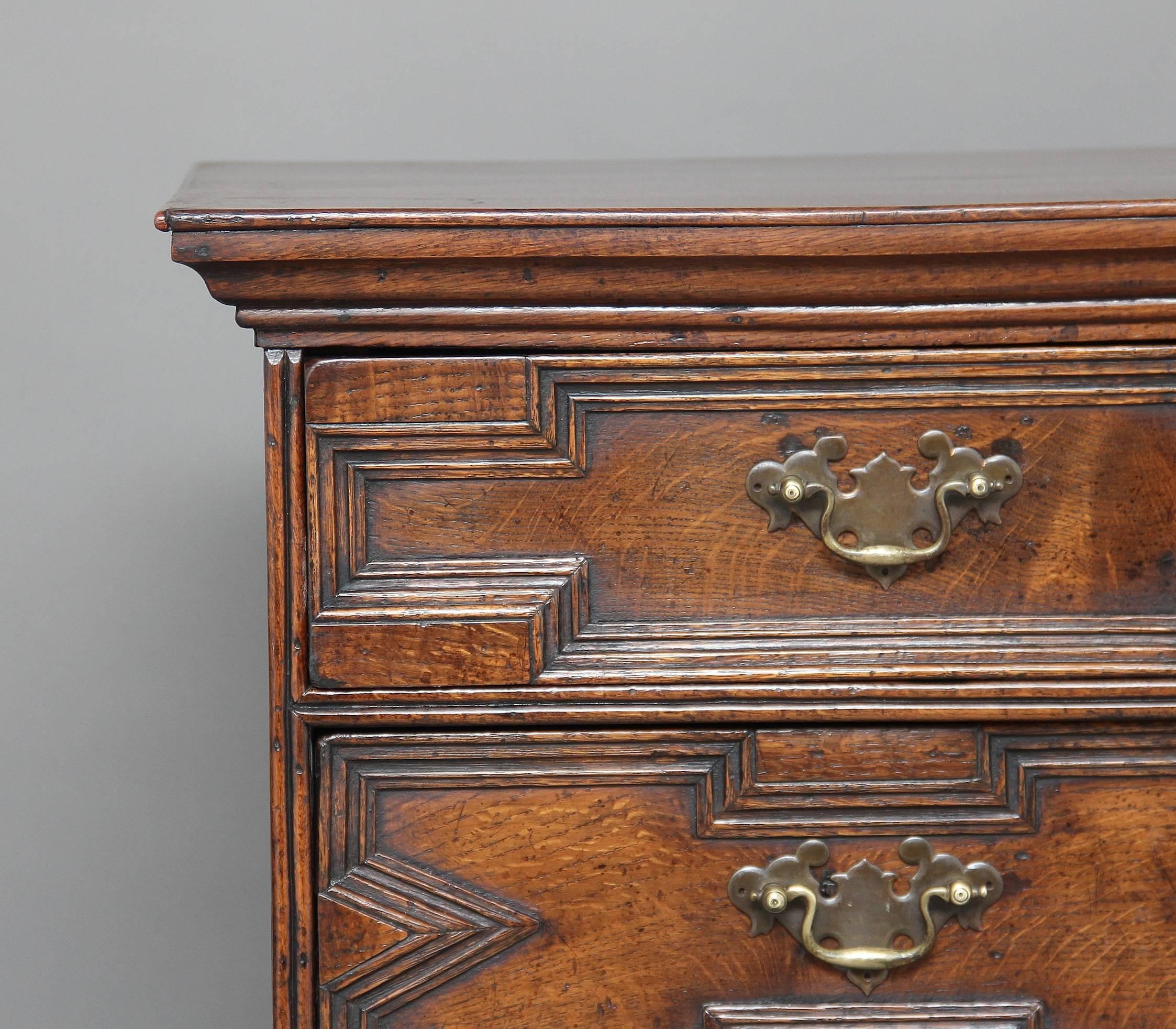 18th century oak geometric chest on stand with double d mouldings, the chest having a stepped cornice above two short over three long oak lined graduated drawers, with brass handles and escutcheons, the base section having a combination of three