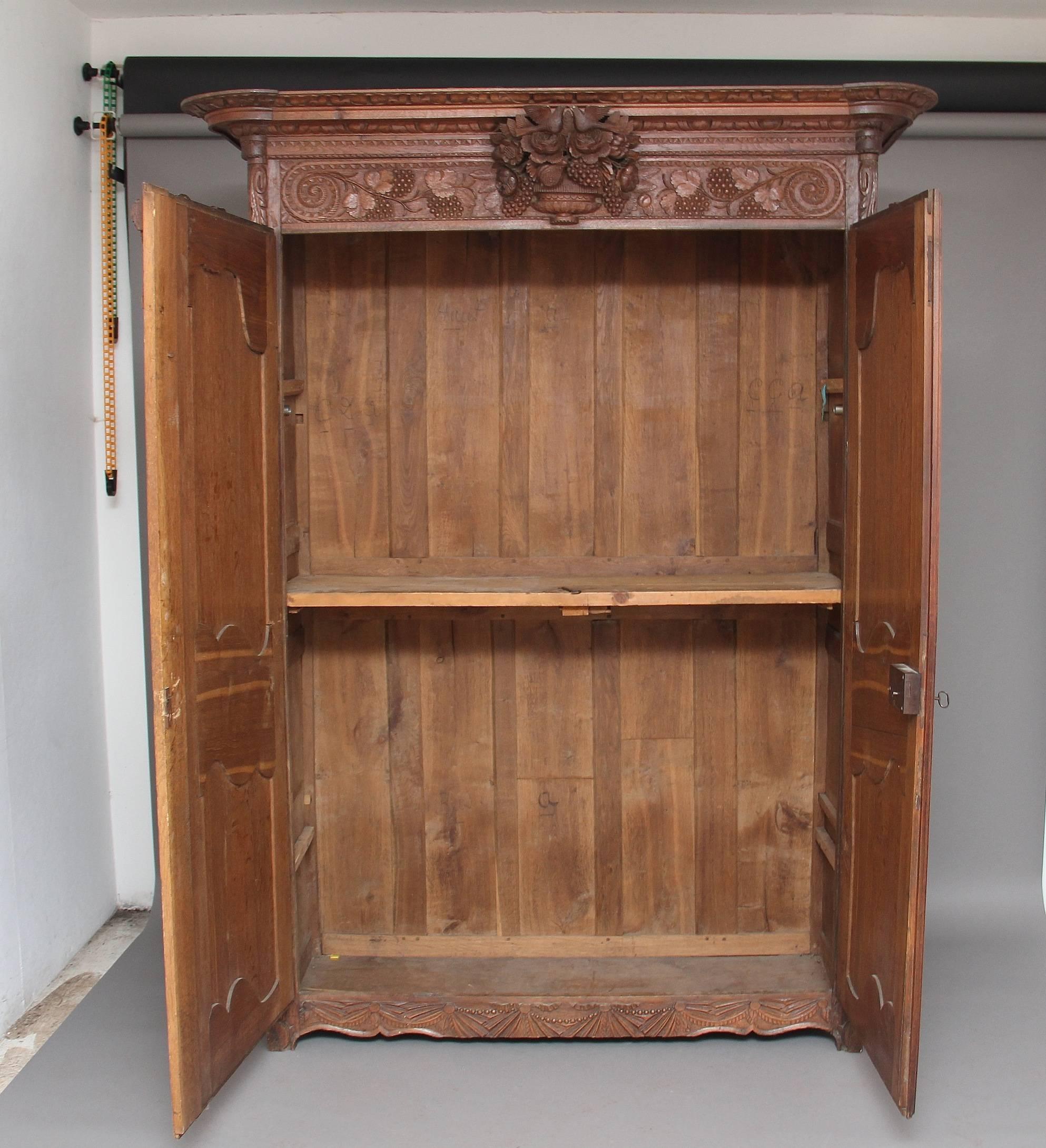 Early 19th century French oak marriage armoire from the Normandy region, the shaped and carved cornice with a frieze below with lovely crisp carvings of two love birds in the centre surrounded by grapes and foliage, the armoire having two doors each