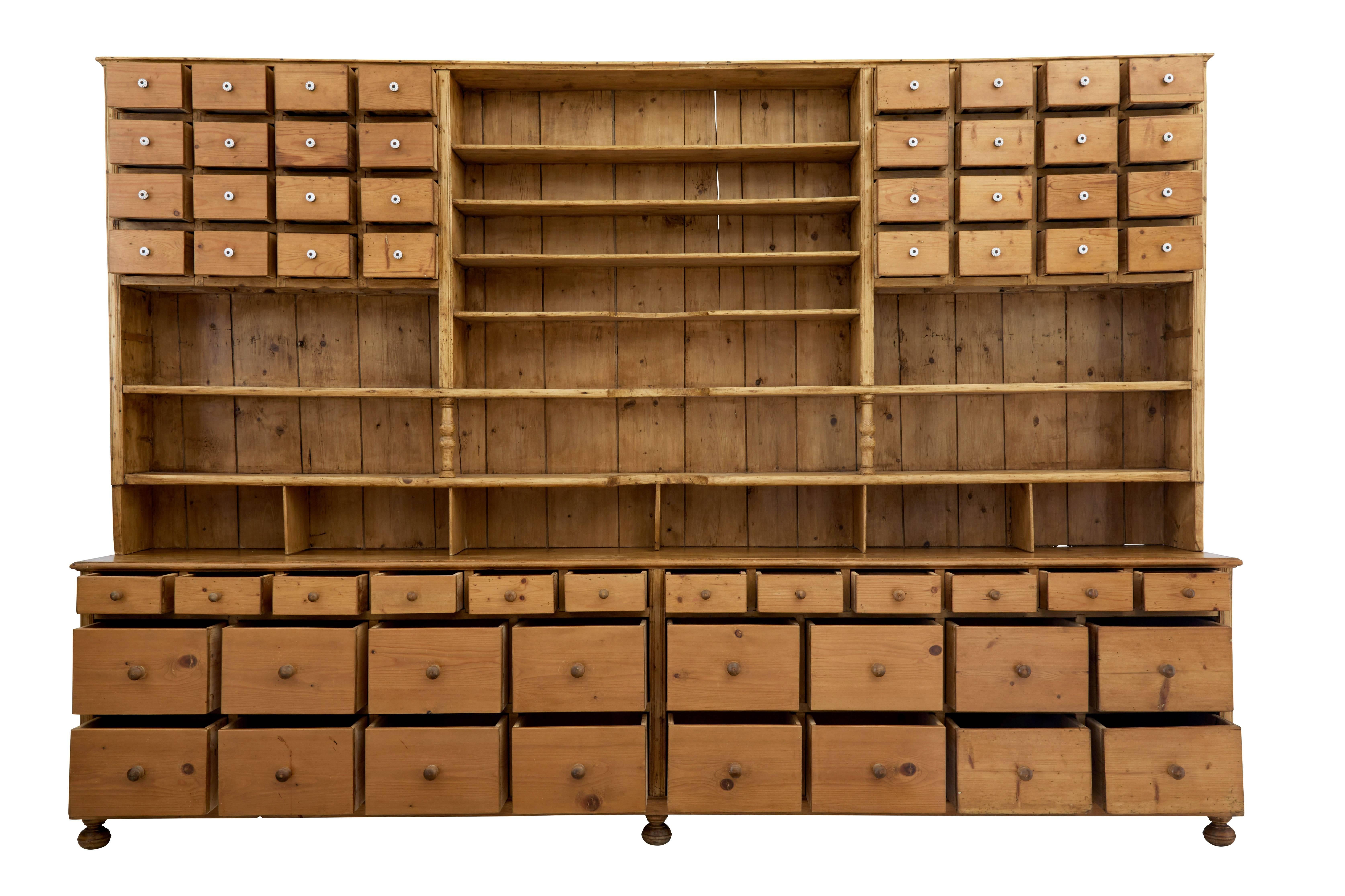 Two-part pine apothecary of large impressive proportions, circa 1880.
Bottom section of 16 large drawers with 12 smaller drawers above these. Top section with a central section of shelves, flanked either side by a bank of 16 drawers.
Wooden