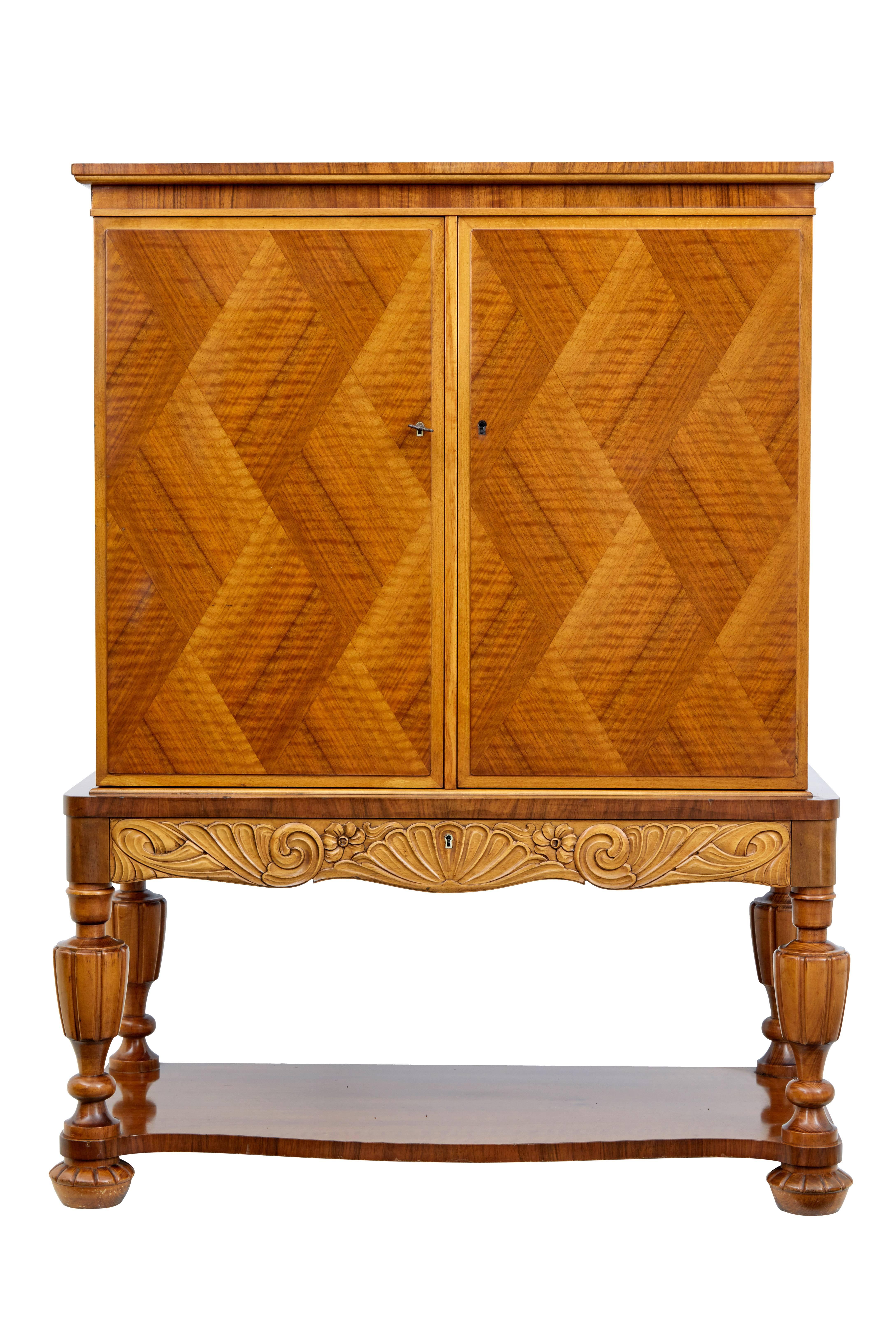 Decorative Art Deco cabinet on Stand circa 1930.
Diamond shaped veneer layout on the doors, with single carved drawer below.
Doors open to a partially fitted interior of 4 shelves and a bank of 3 drawers.
Standing on 4 baluster legs united by