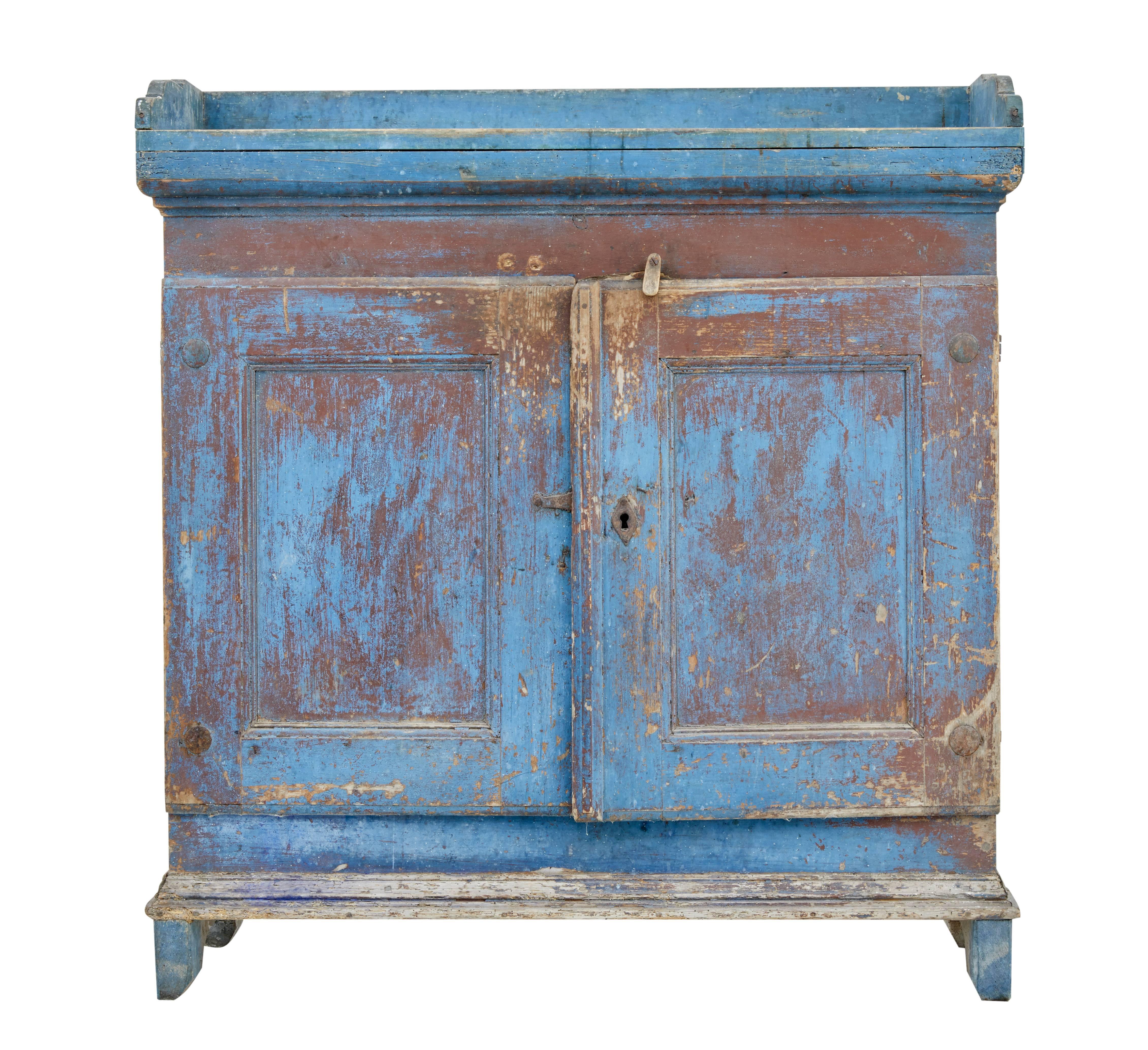 Here we offer a rustic Swedish painted cupboard, circa 1800.
In original rustic condition with the various of layers of paint wearing through the plain pine.
Top surface with gallery, double doors open to reveal three shelves and original